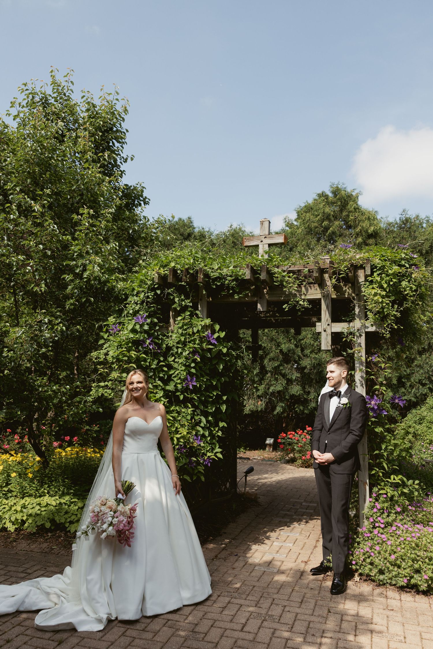Wedding couple poses for photos in a beautiful garden courtyard with brick pathway and pergola.