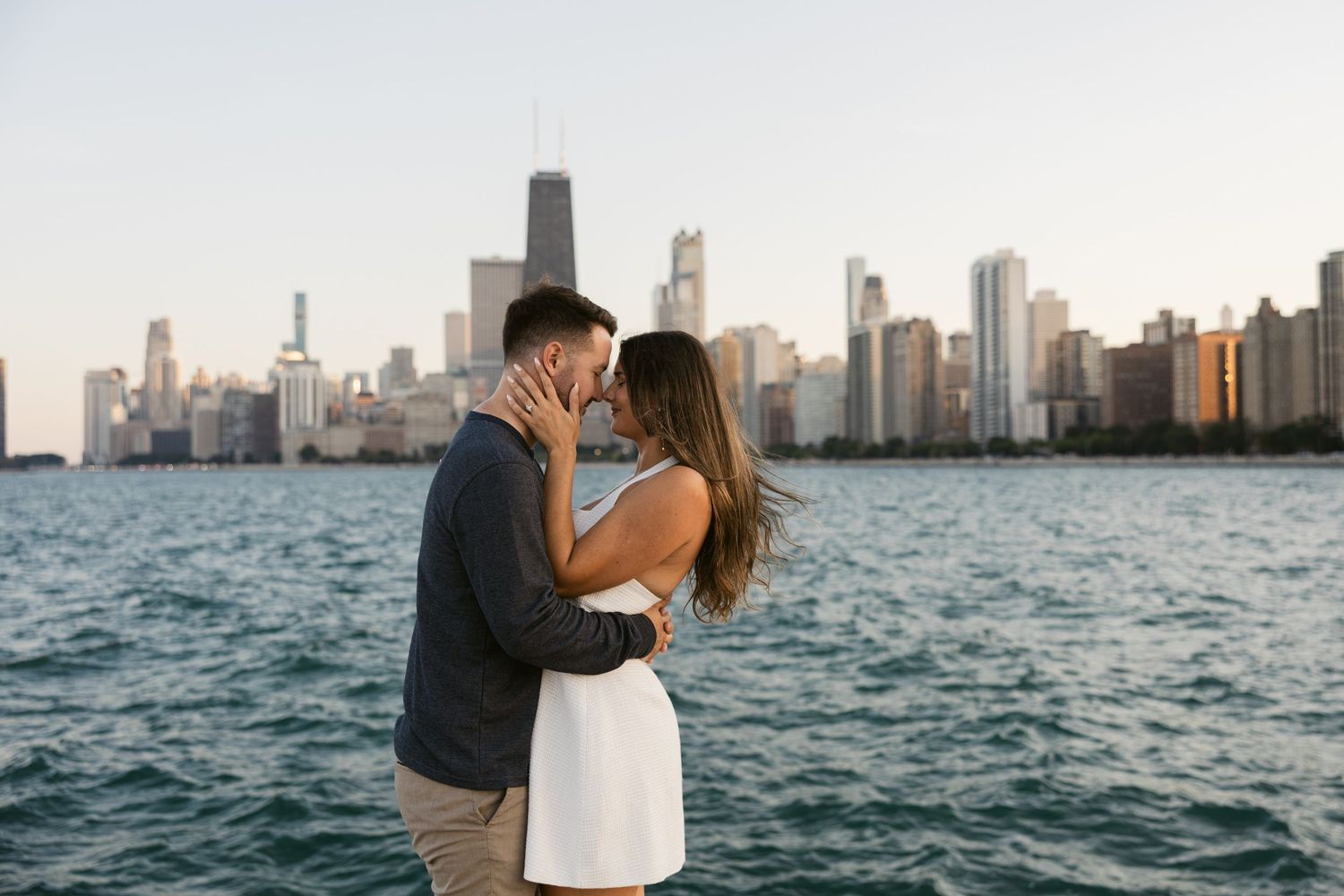 A couple embraces along the waterfront with Chicago's iconic downtown skyscrapers rising in the background.