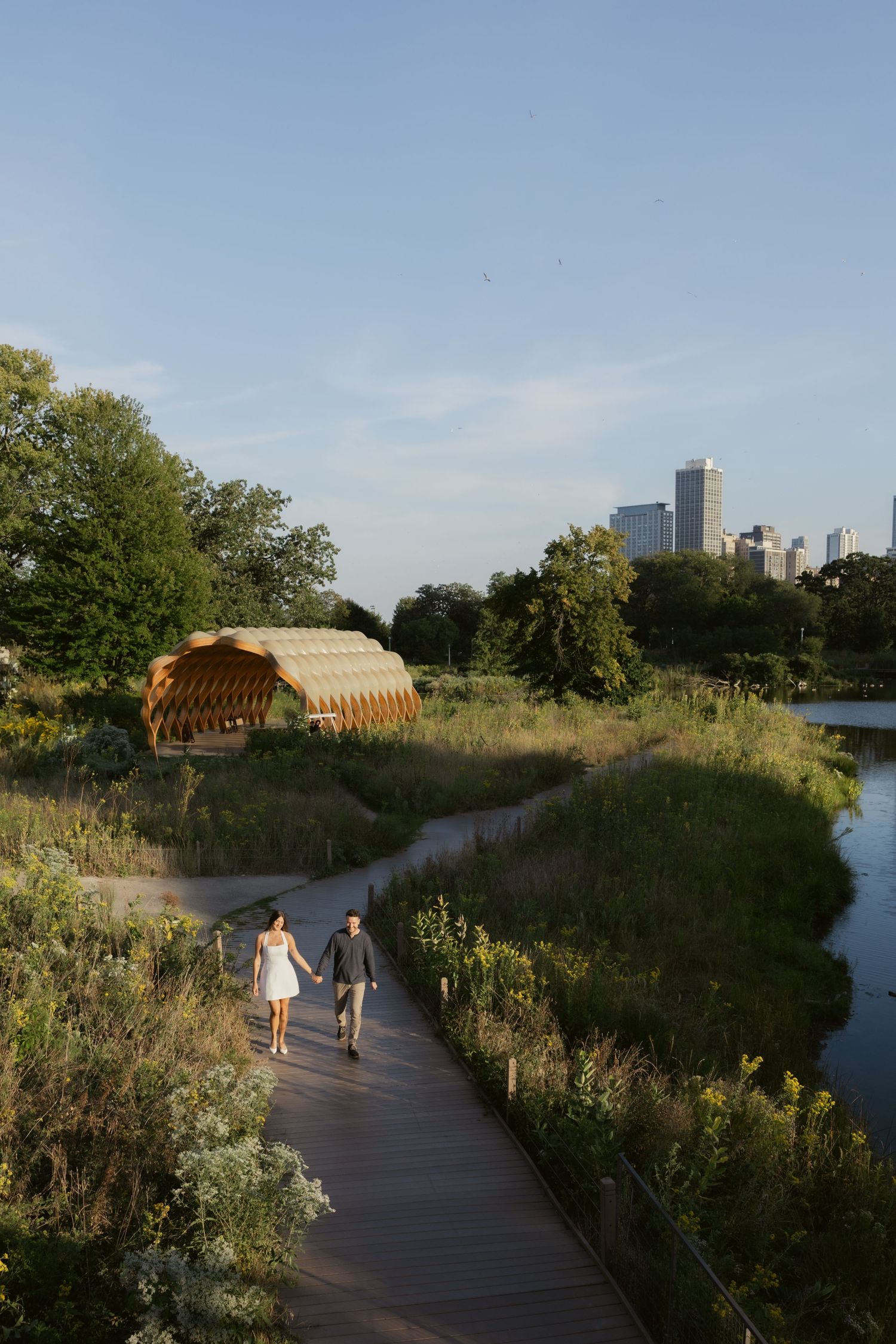 Wooden boardwalk path leading through natural wetlands with city skyline visible in the distance.