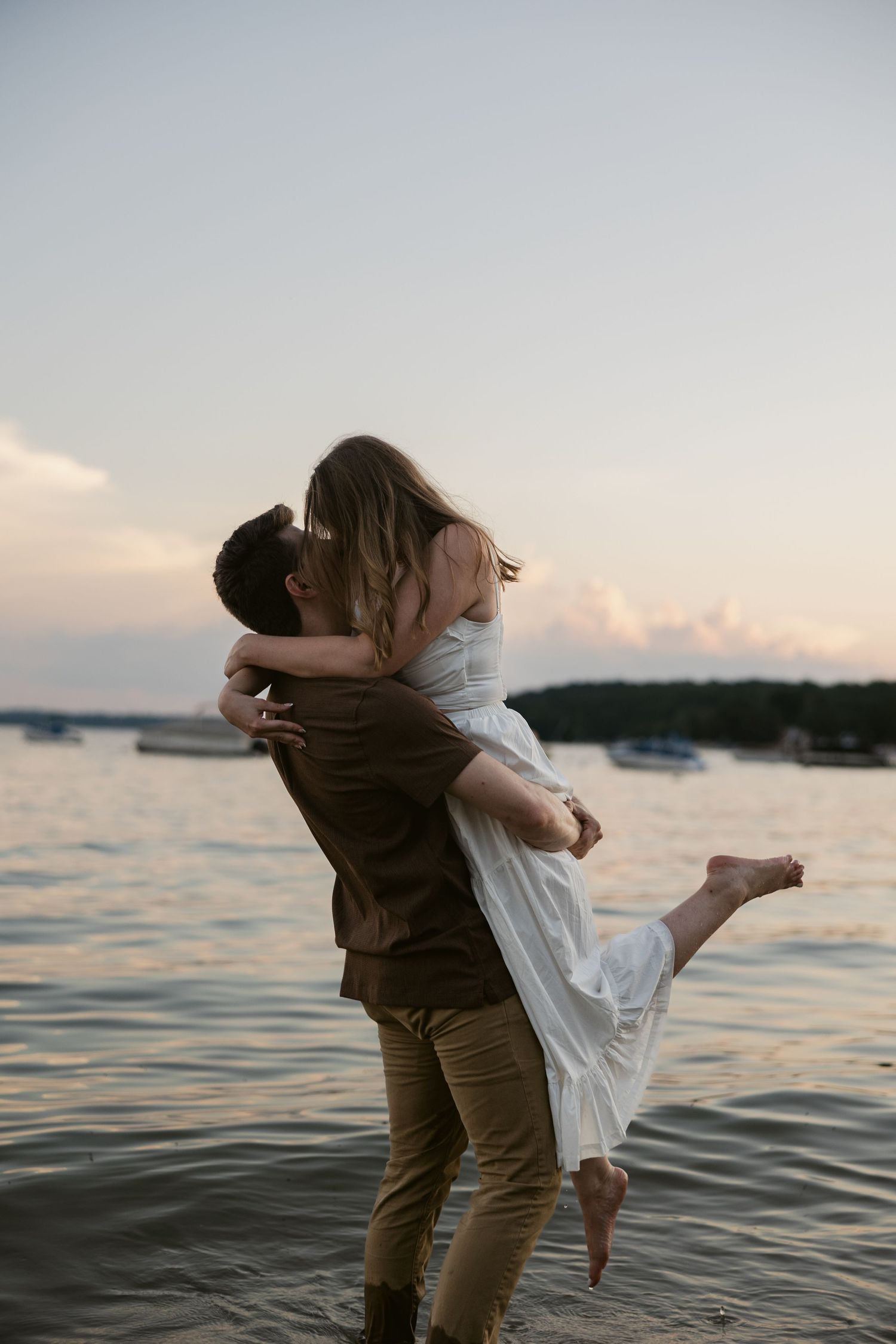 Romantic couple embracing and dancing by the water during sunset.