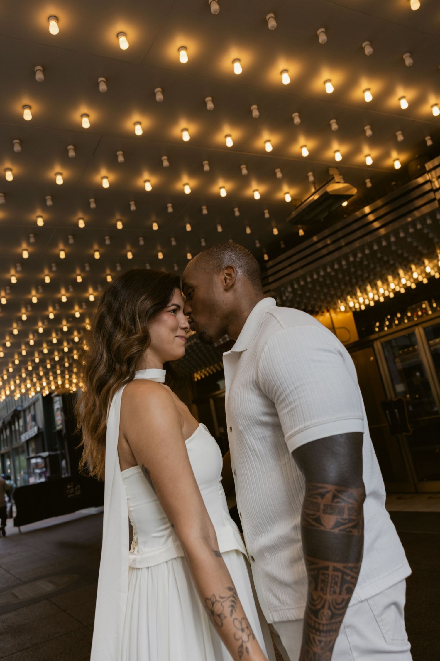 A couple embraces under twinkling lights in matching white outfits.
