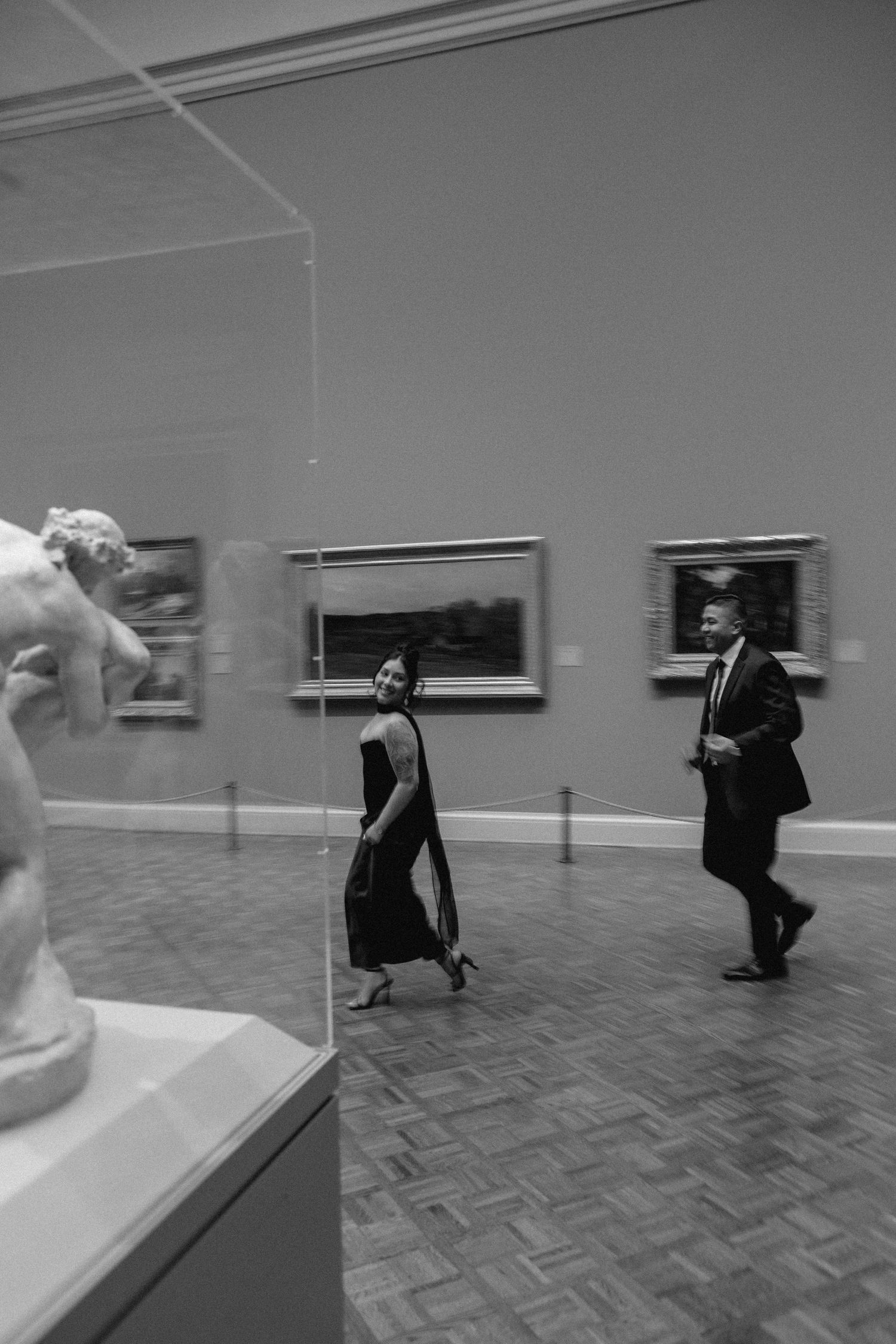 A sequence of black and white photos showing a figure moving through an art gallery with white walls.