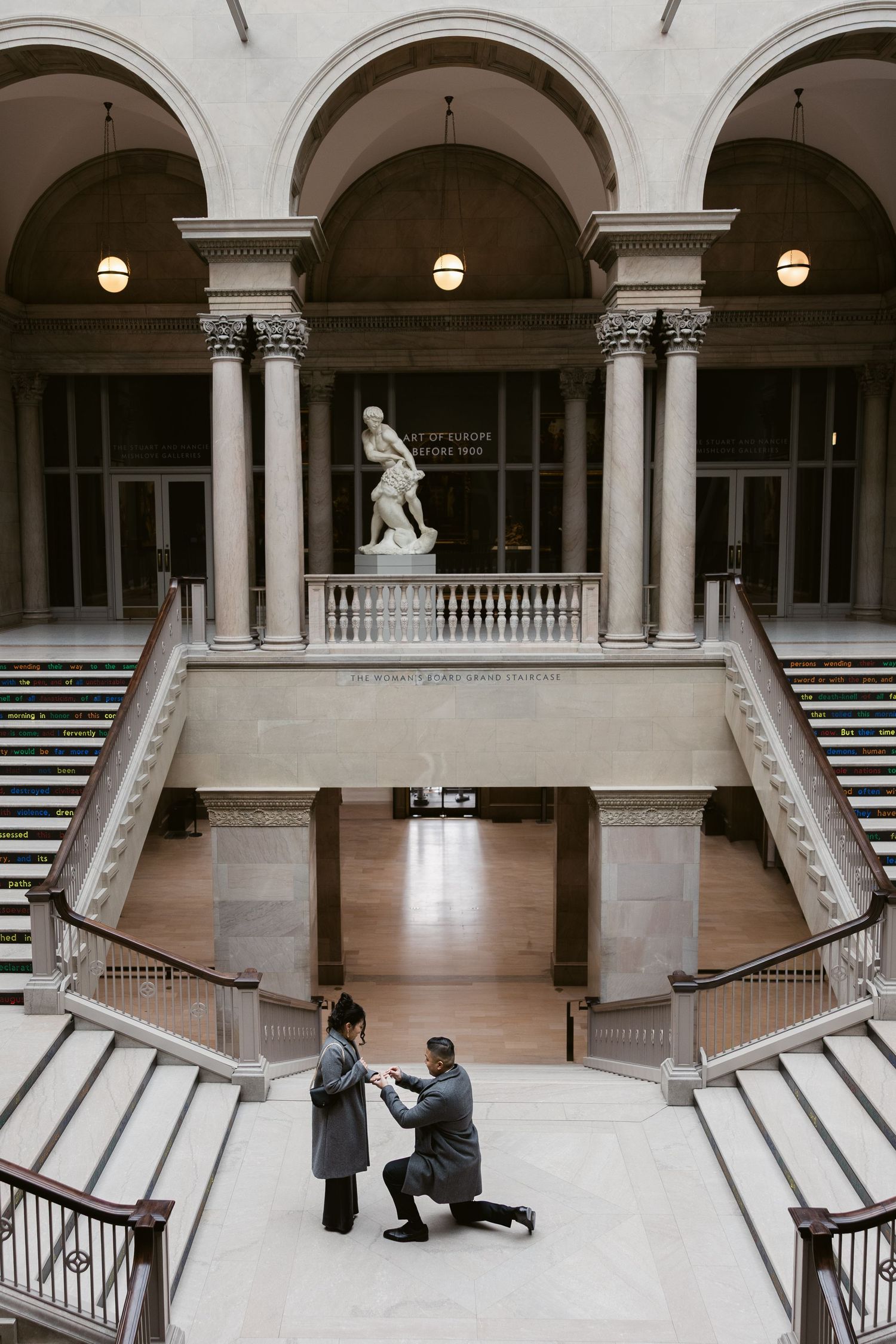 A grand marble hall with arched colonnade and symmetrical staircases.