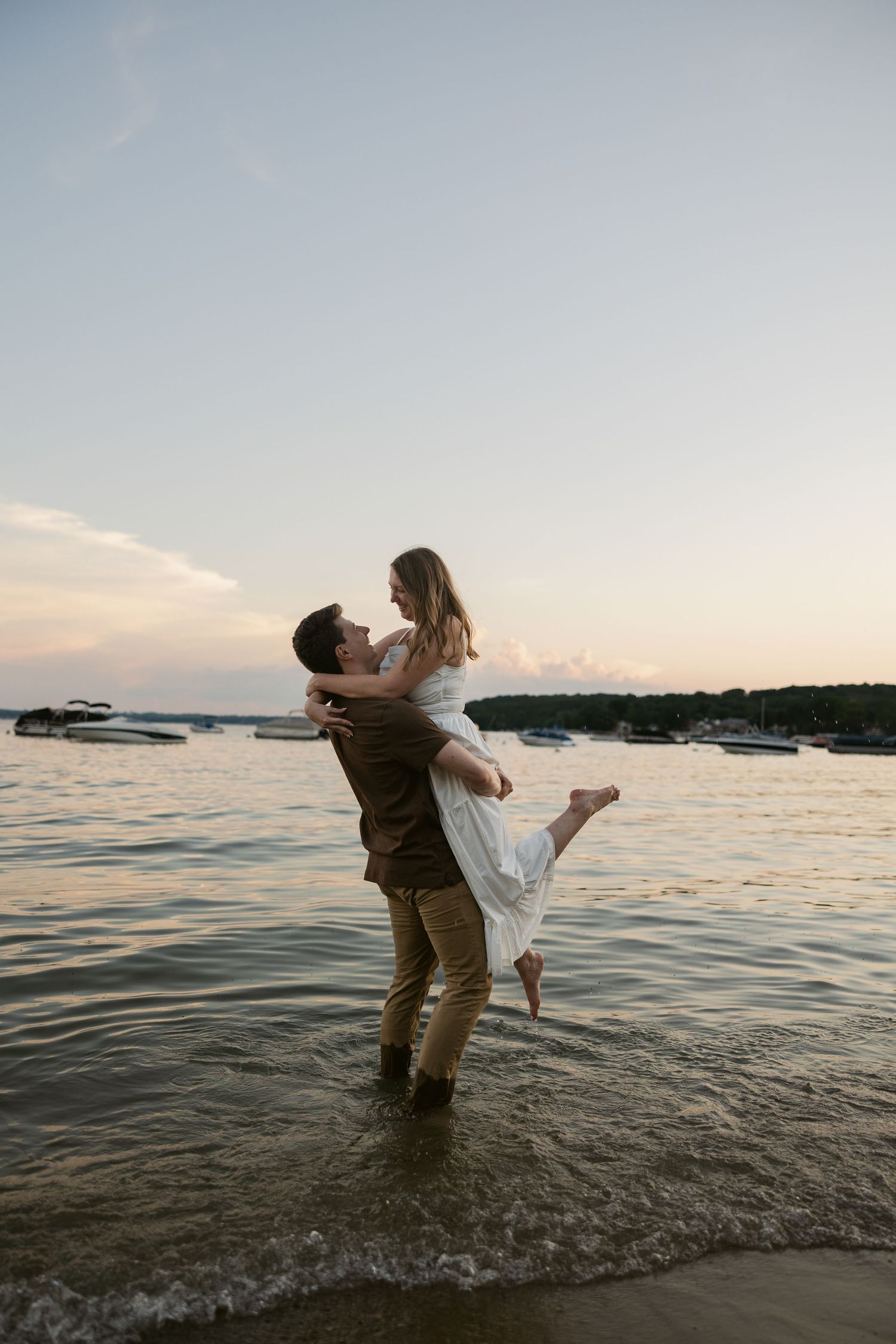 A couple splashes and plays together in the ocean water during sunset.