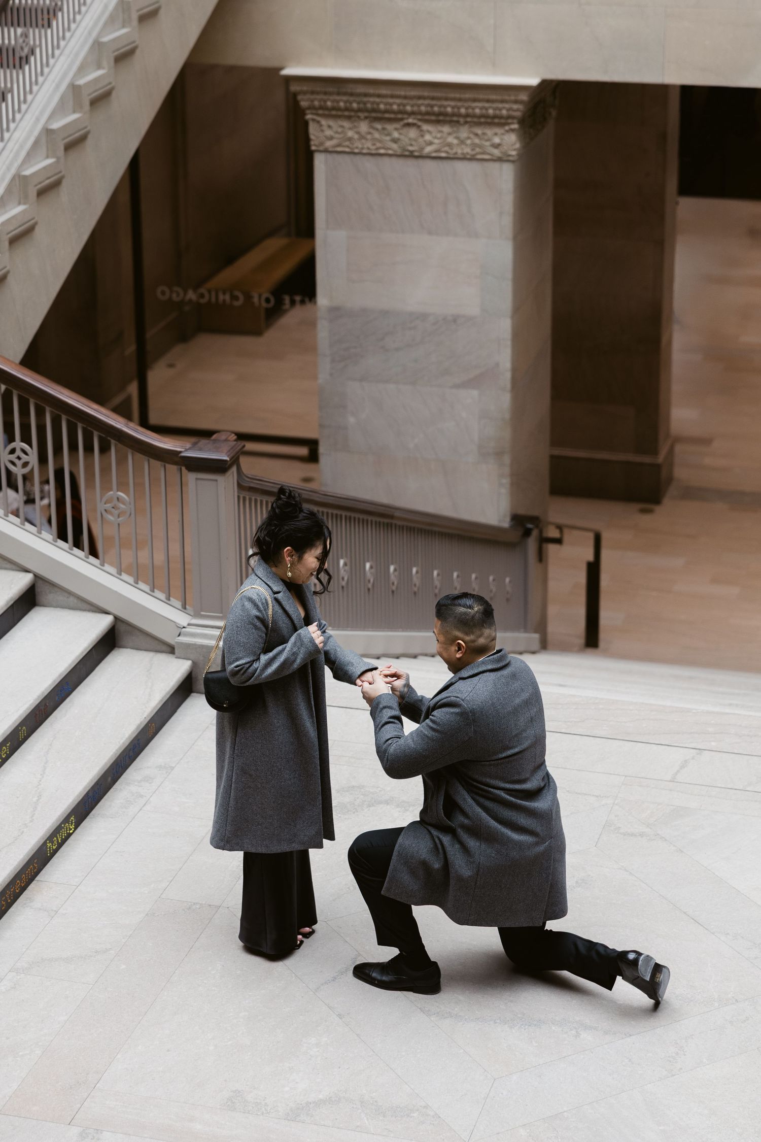A couple sharing an intimate moment on a marble floor in front of a grand staircase.