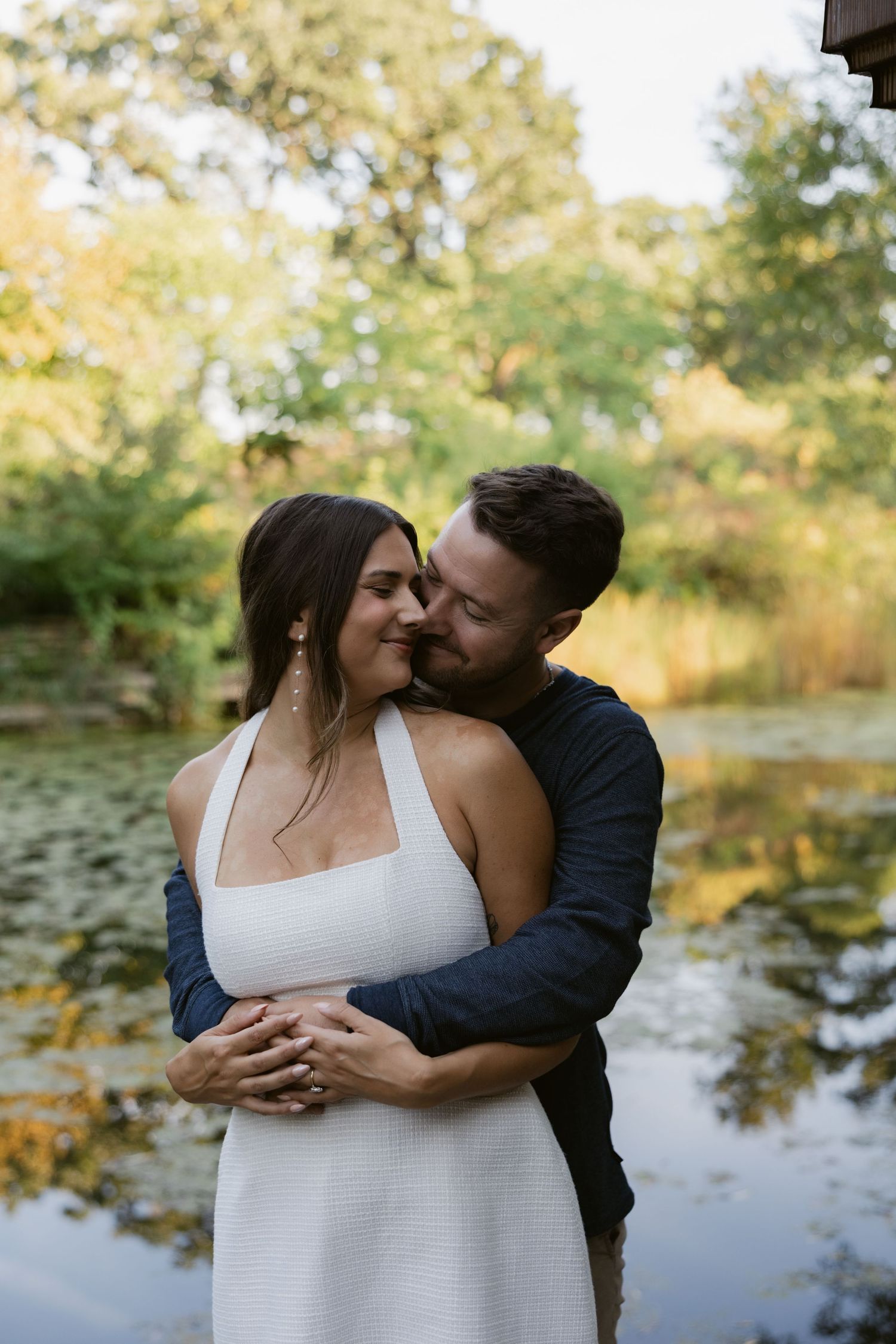 Intimate outdoor photo session with couple embracing near a peaceful pond.