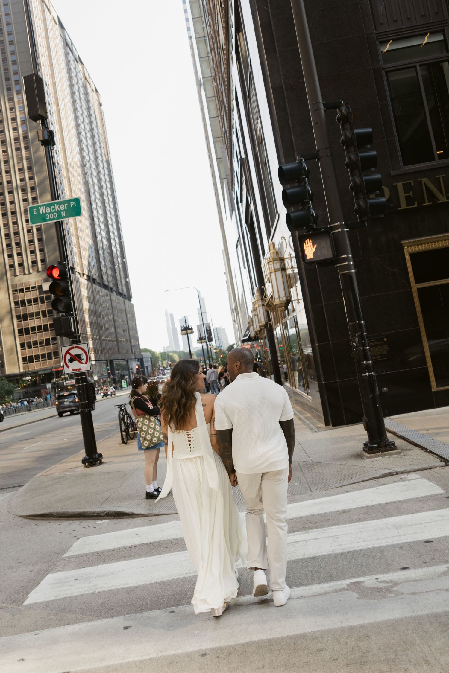 A couple in white outfits walking on a city street with tall buildings in the background.