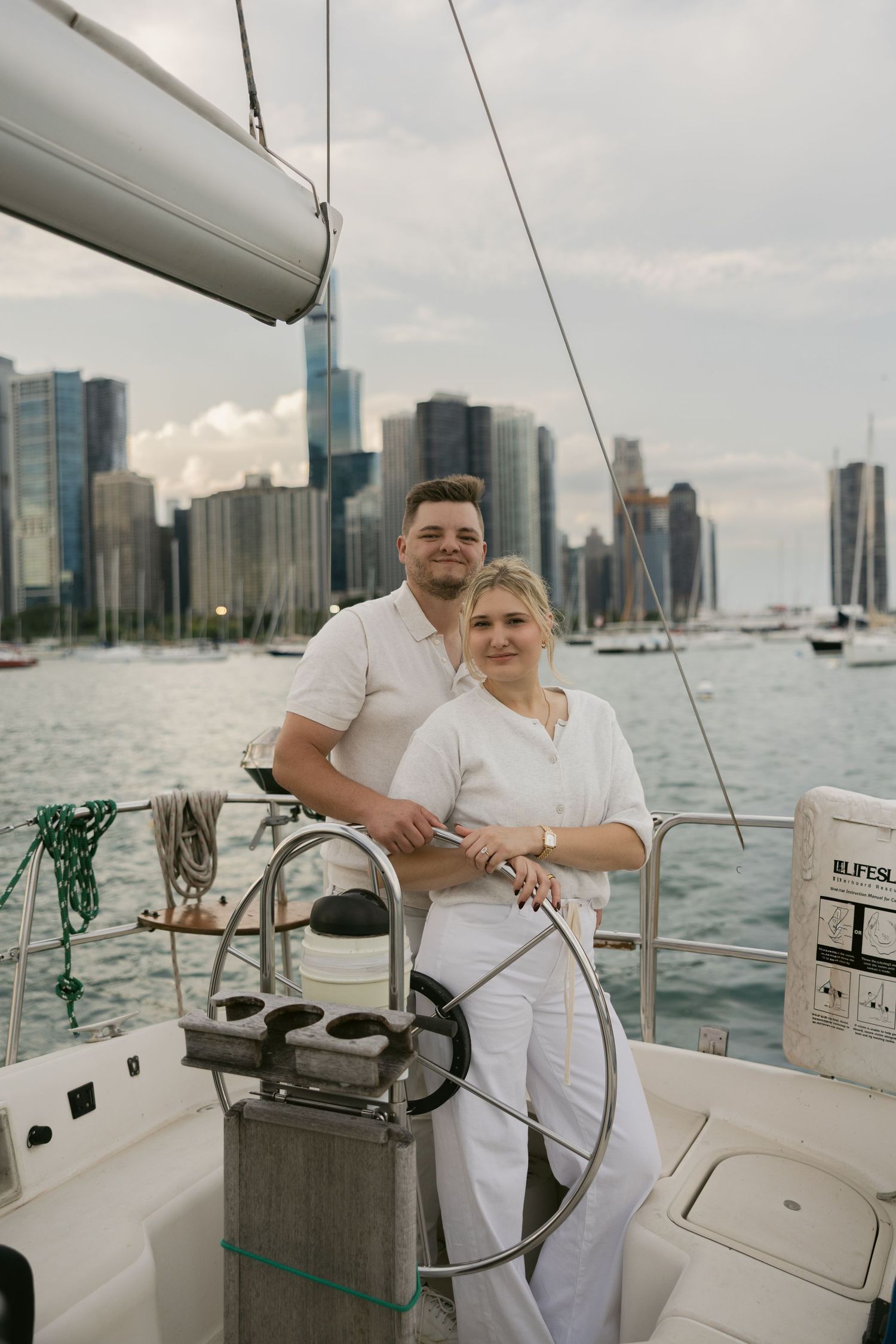 Couple navigating sailboat together with Miami skyline visible across the water.