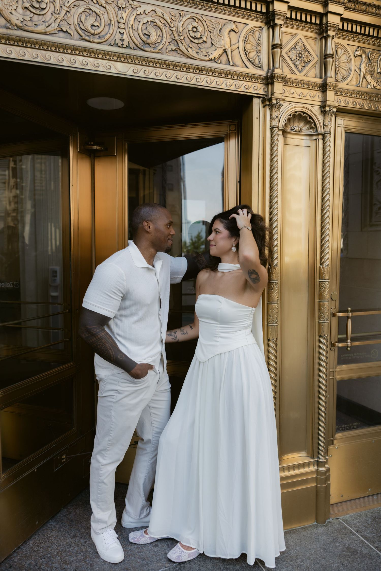 A couple shares a playful moment in front of an ornate gold-detailed building entrance.