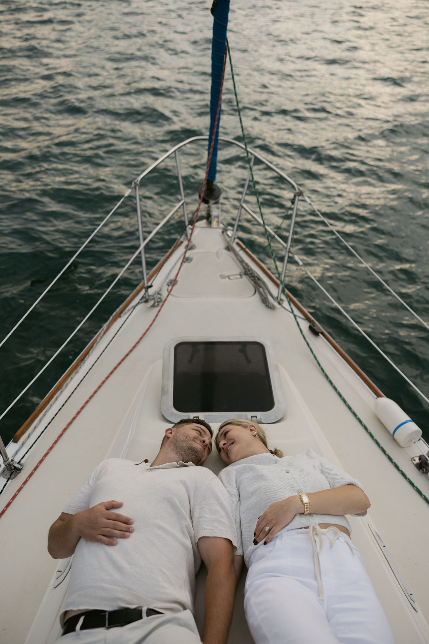 Couple sharing tender moments on bow of sailboat at sunset.