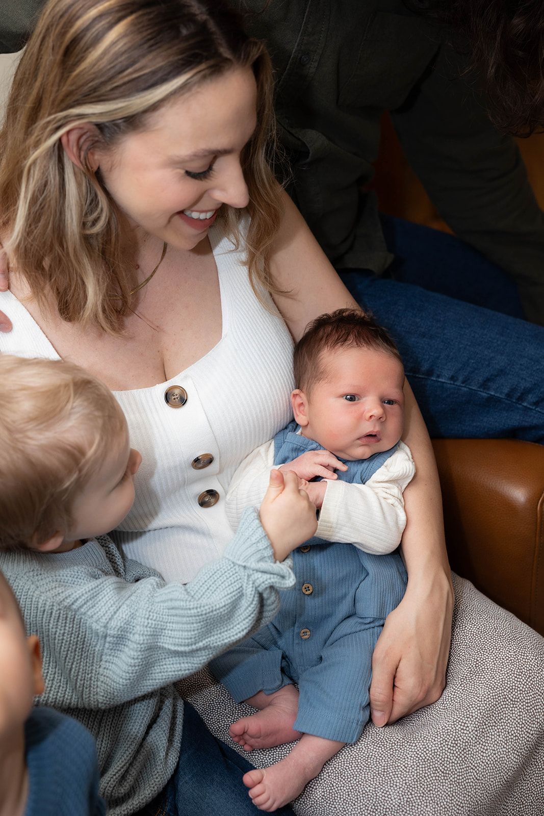 Mother and young child bonding with newborn baby on couch.