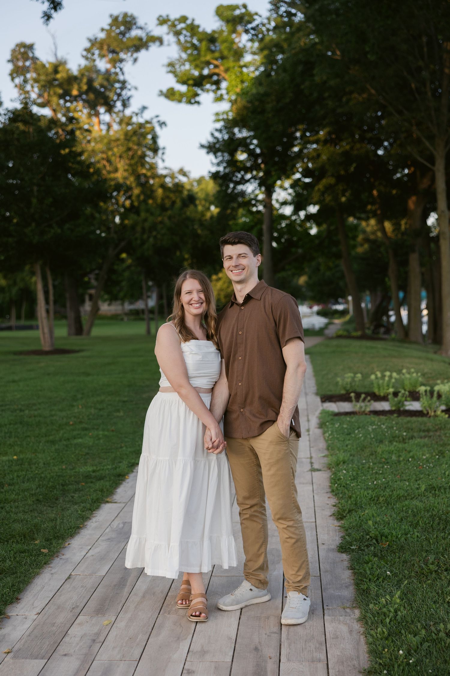 A couple stands on a wooden deck in a park setting during golden hour.