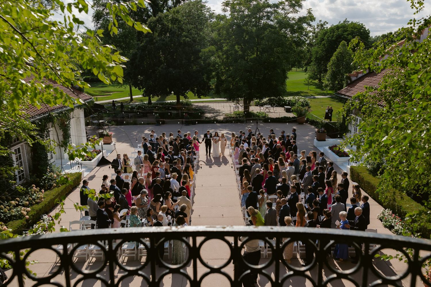 Large crowd of graduates gathered on a scenic garden pathway during an outdoor commencement ceremony.
