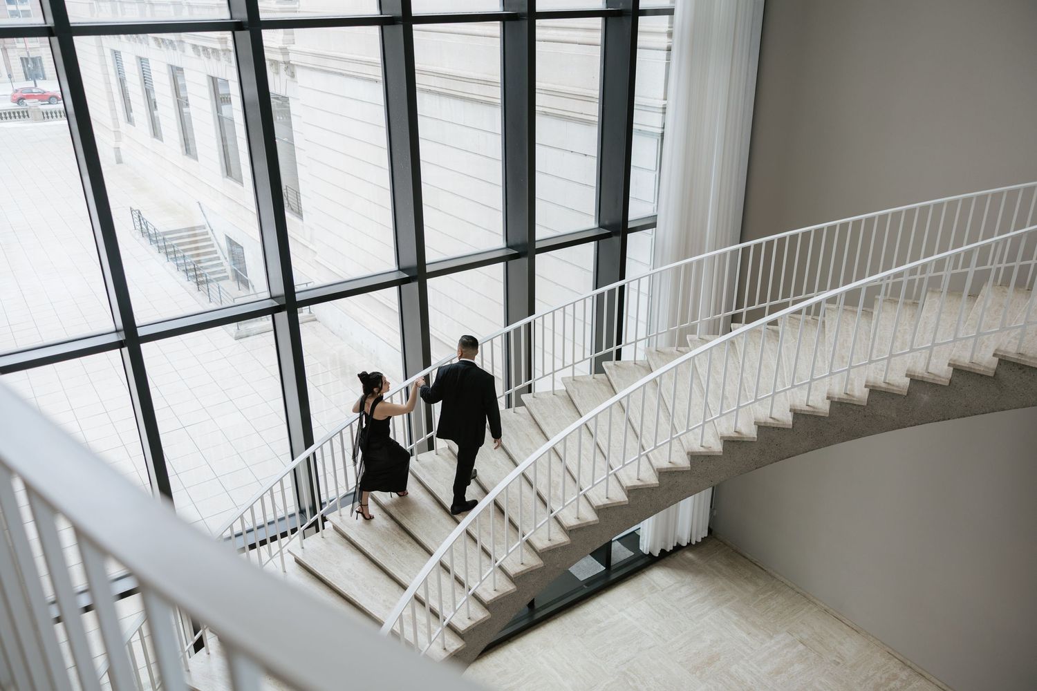 Modern interior staircase with white railings and large windows in minimalist design.