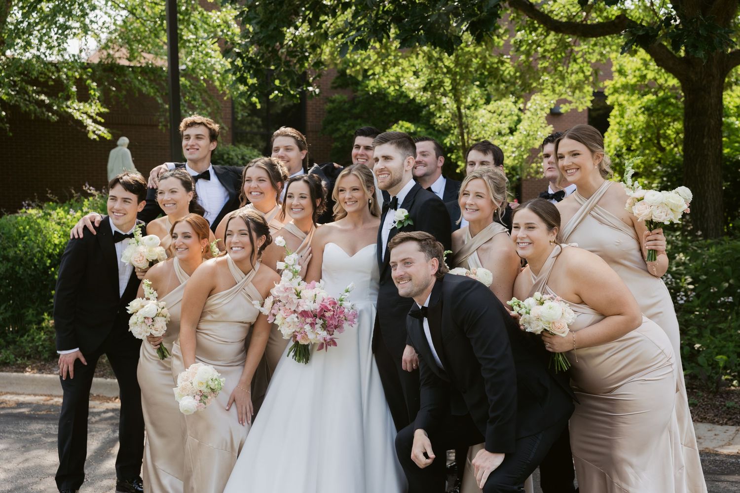 Wedding party poses outdoors for group photos in a beautiful garden setting.