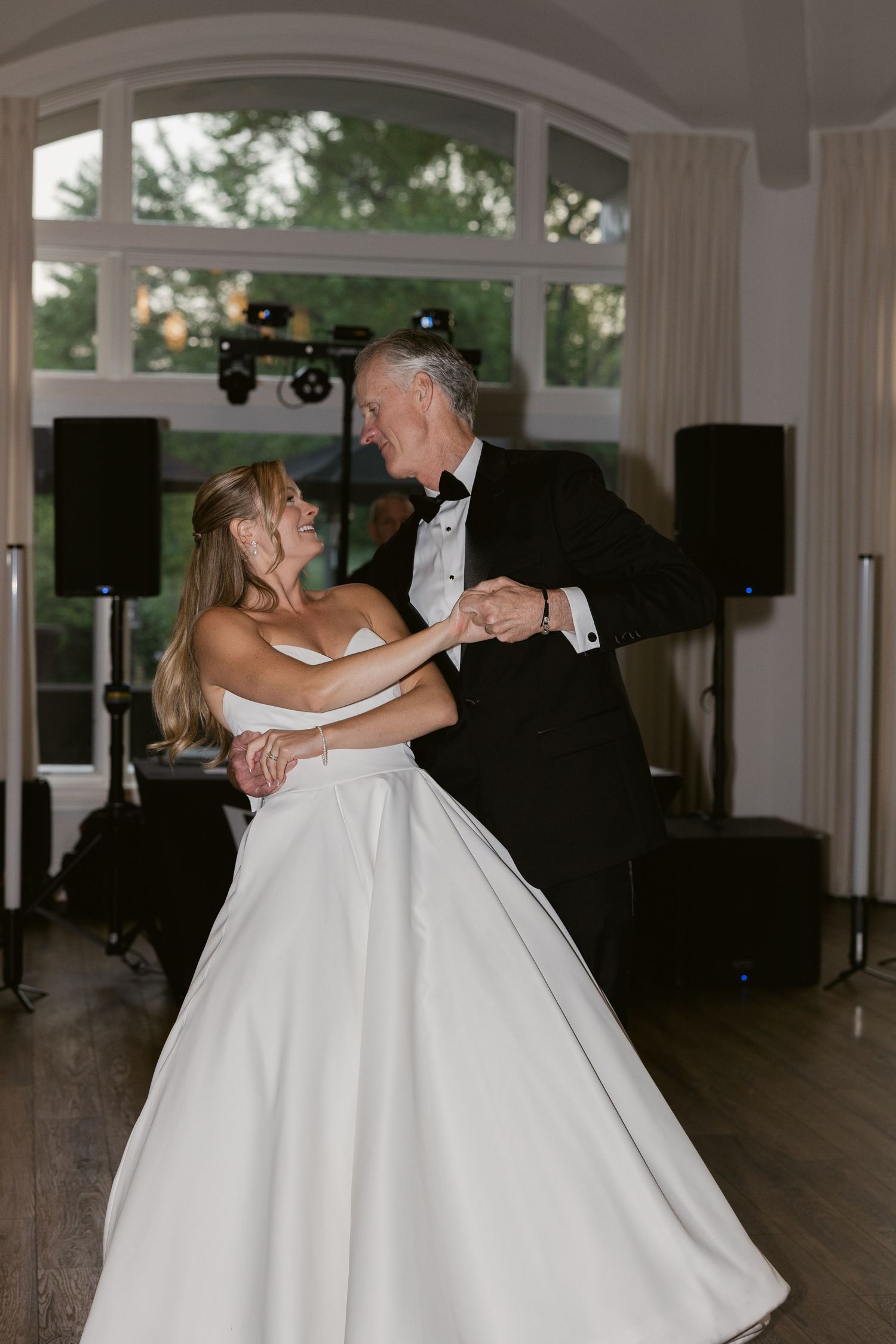 Couple shares their first dance in elegant ballroom with arched windows.