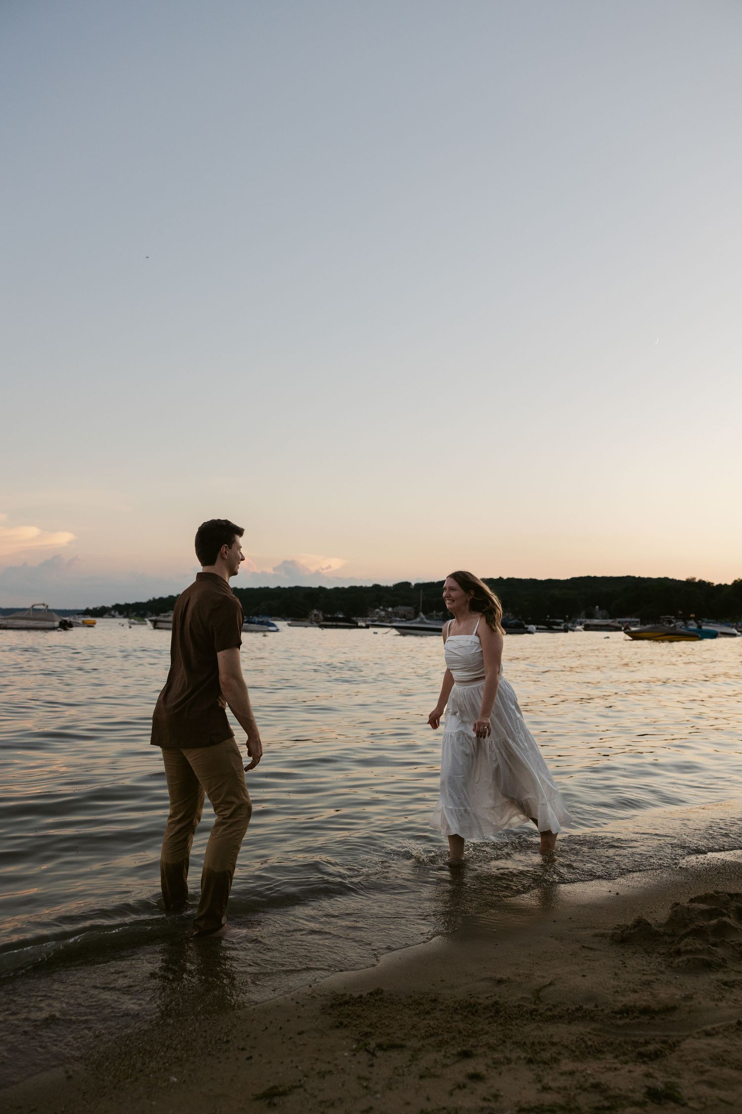 Silhouetted couple walks through shallow water during sunset at beach.