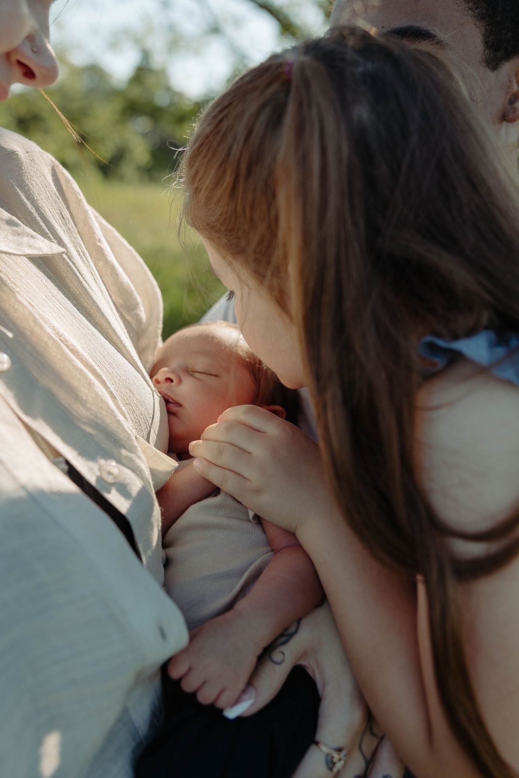Intimate moment of parents cradling newborn baby outdoors in natural lighting.