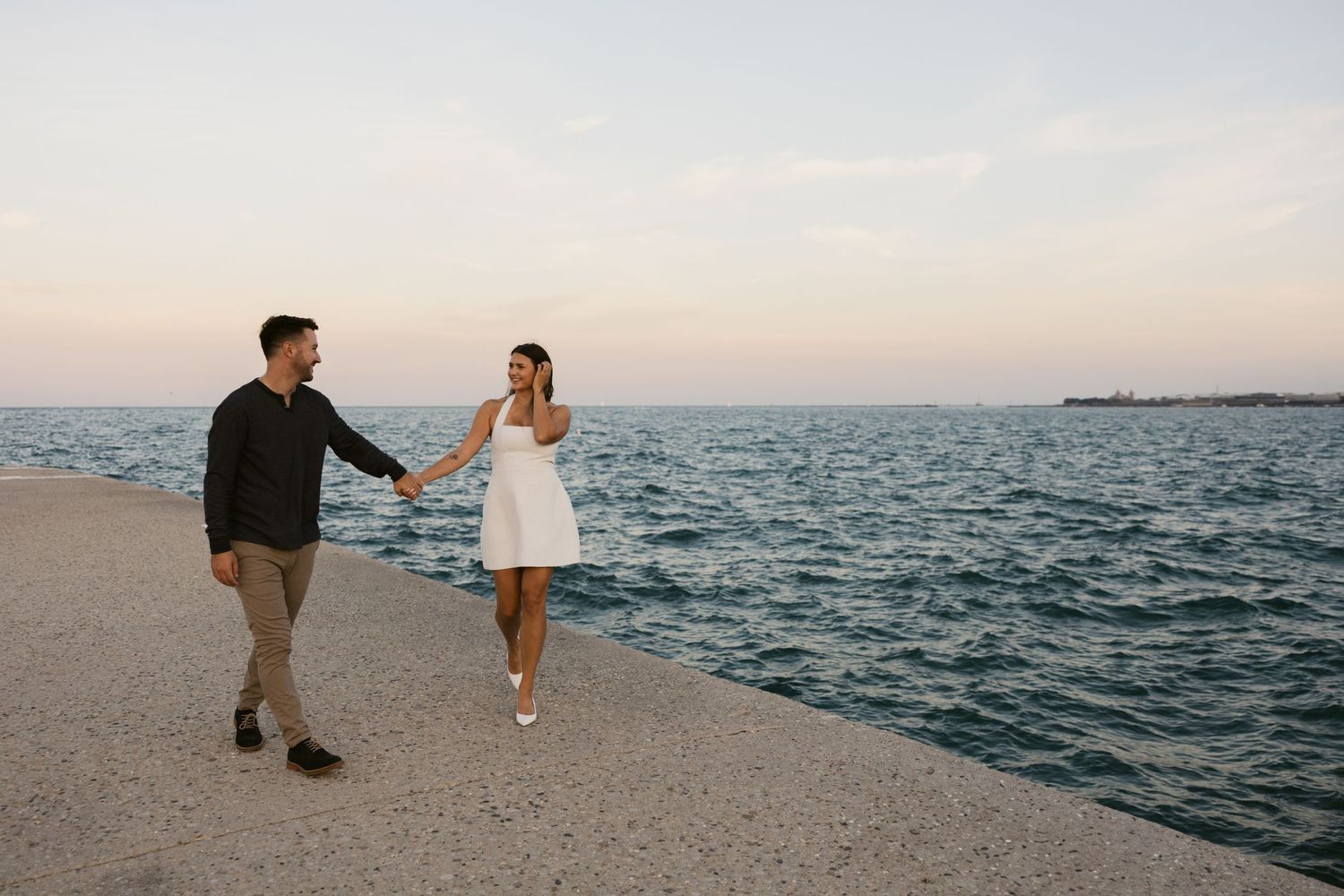 Panoramic view of a couple strolling along Lake Michigan with Chicago's skyline visible.