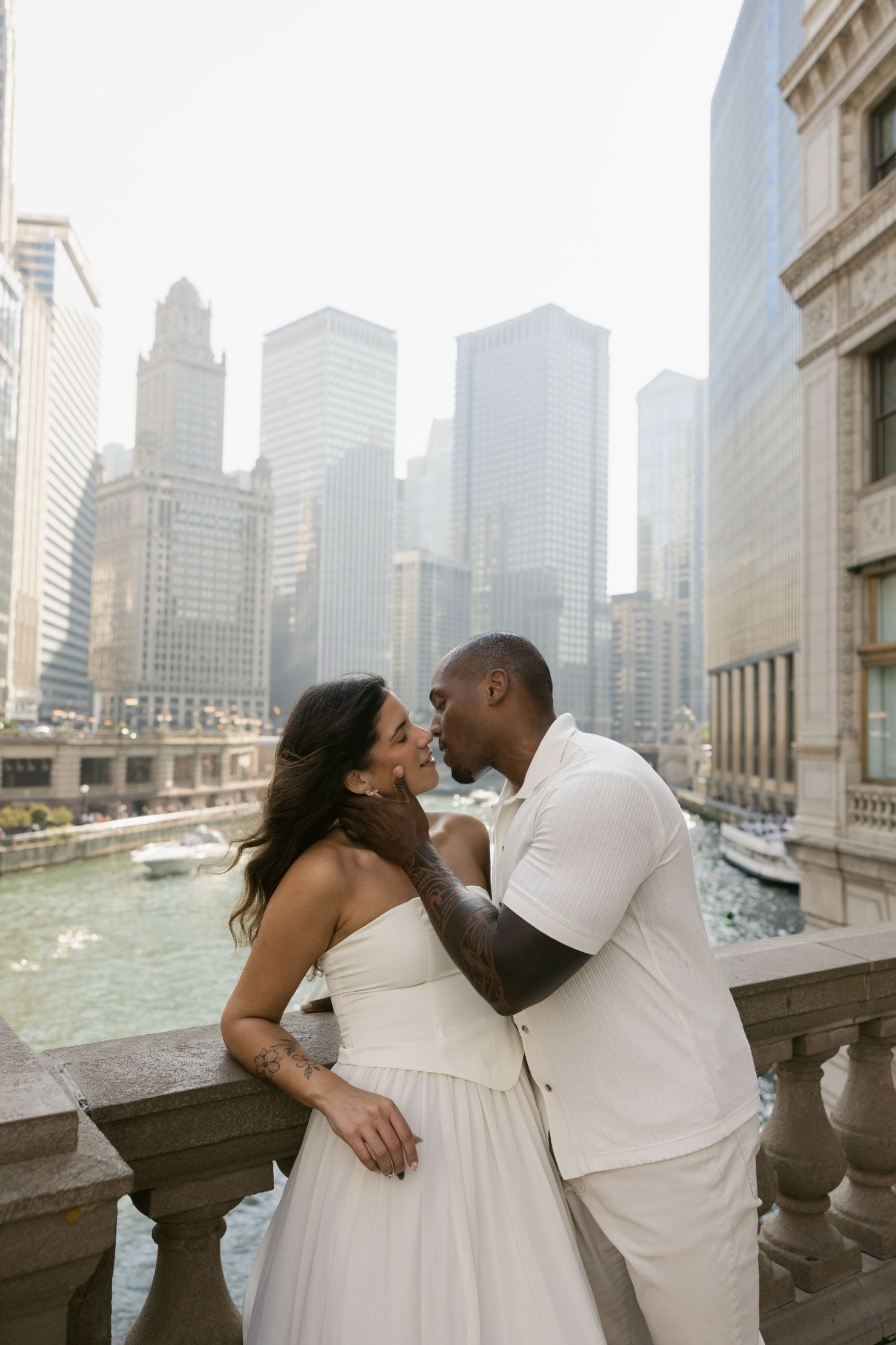 A couple in white attire embraces on a balcony with Chicago's iconic skyline in the background.