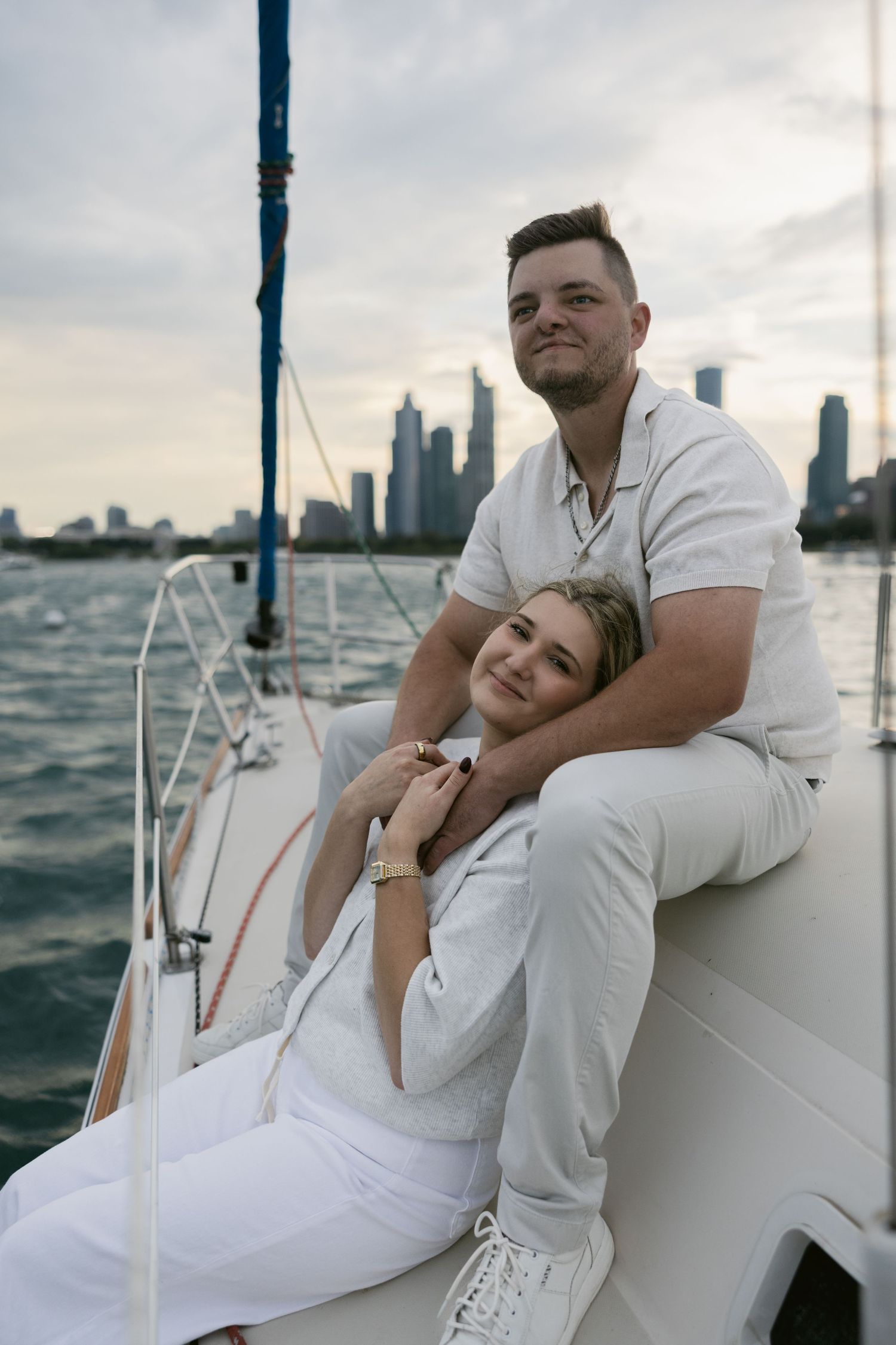 Romantic couple in white outfits sharing intimate moments on a yacht with city skyline in background.