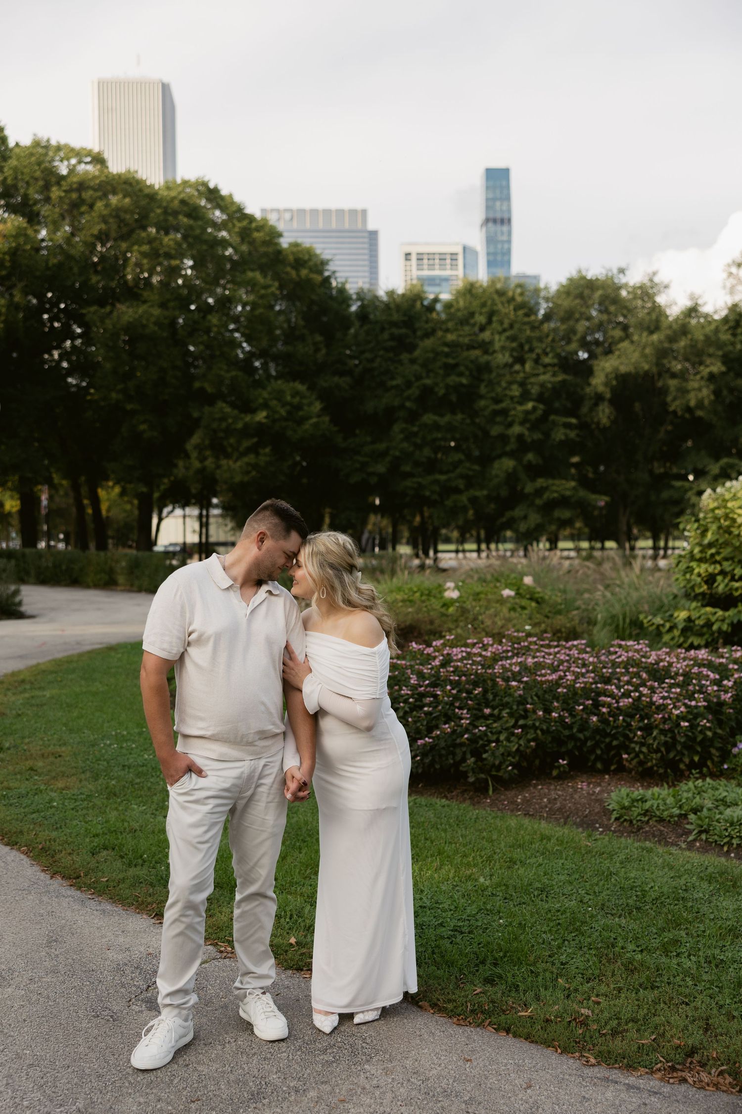 A romantic couple strolls by a garden path with the Chicago skyline visible in the background on their wedding day.