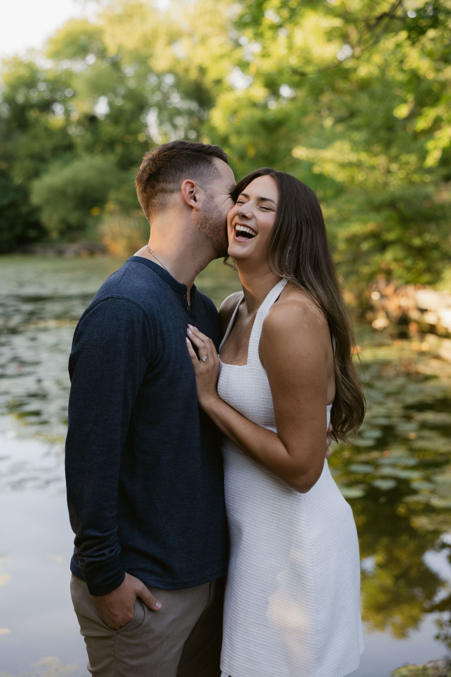 Romantic moment captured by a pond with lush greenery and water lilies in the background.