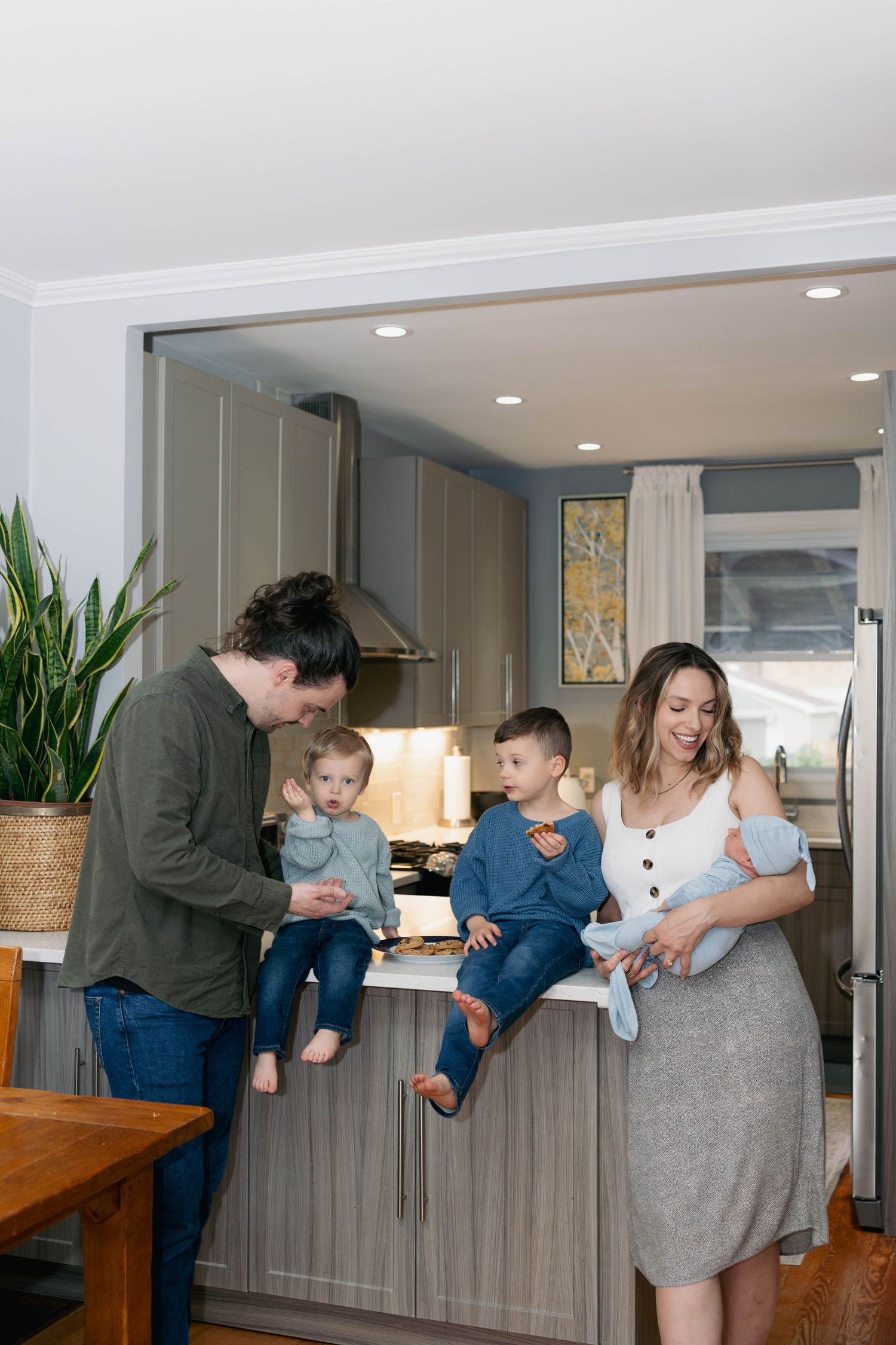 Family gathering in modern kitchen as parents hold children on counter while sharing a casual moment together.