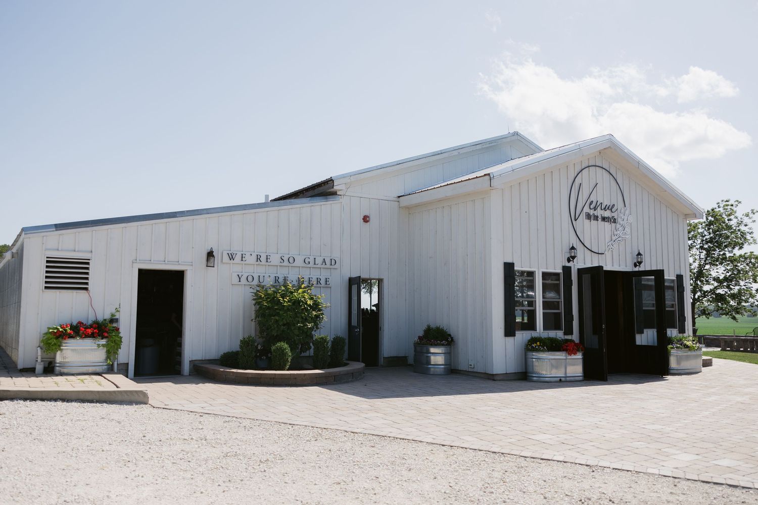 Modern white industrial building with curved metal roof and rustic wine tasting entrance in rural setting.