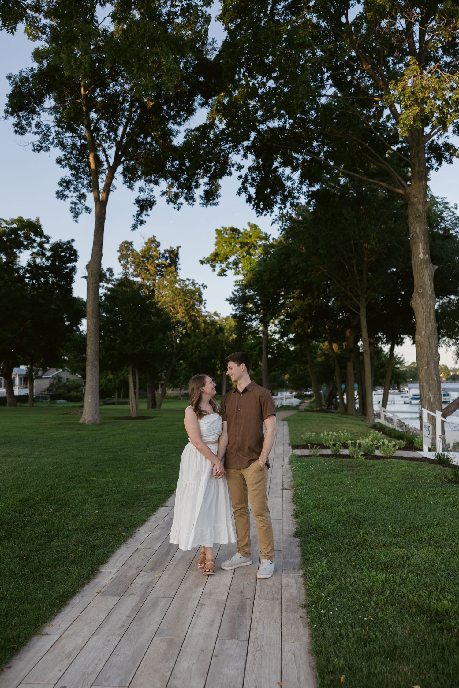 Couple strolls along a tree-lined pathway in a scenic park during golden hour.
