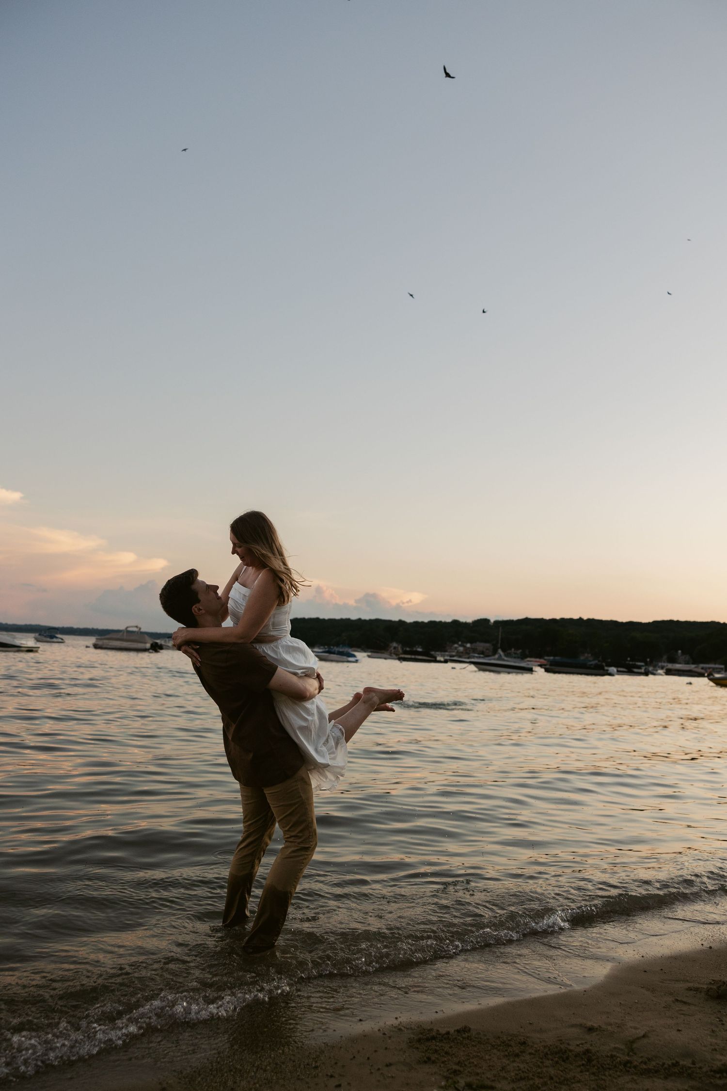 A couple dances and splashes together in the ocean water during sunset, creating a romantic silhouette against the horizon.