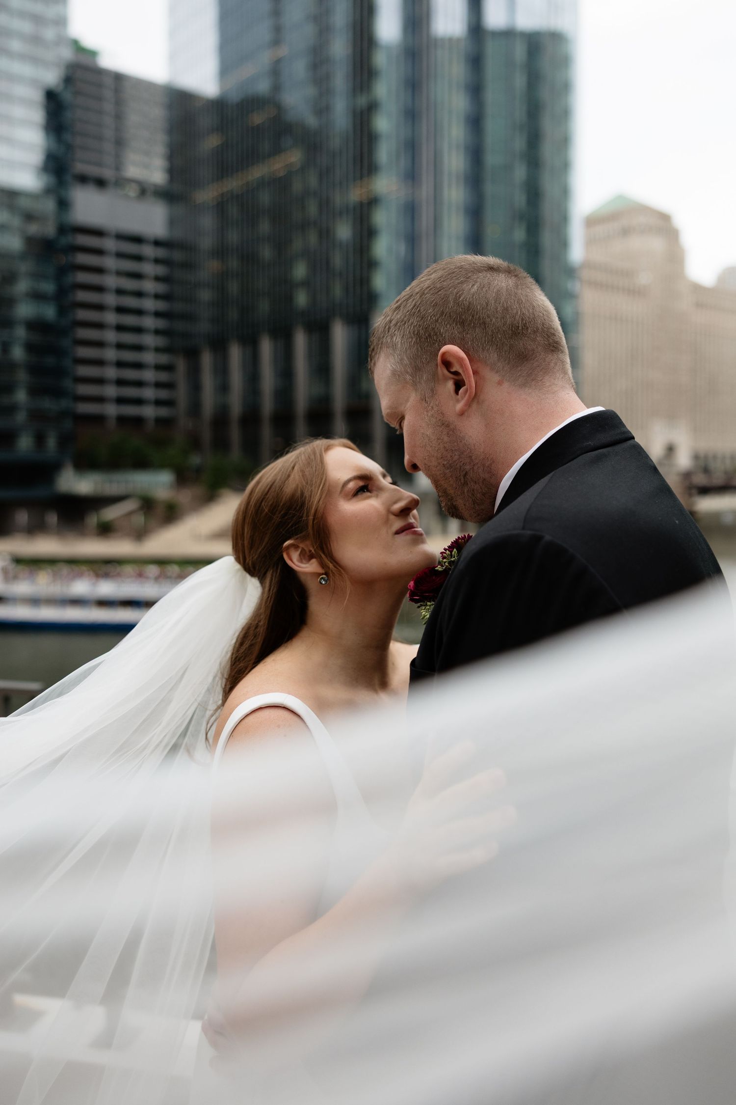 A romantic wedding moment captured against a cityscape backdrop with flowing veil in motion.