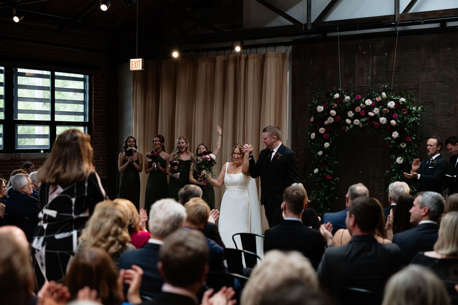 Wedding ceremony guests seated in dark venue with ambient lighting and floral decorations.