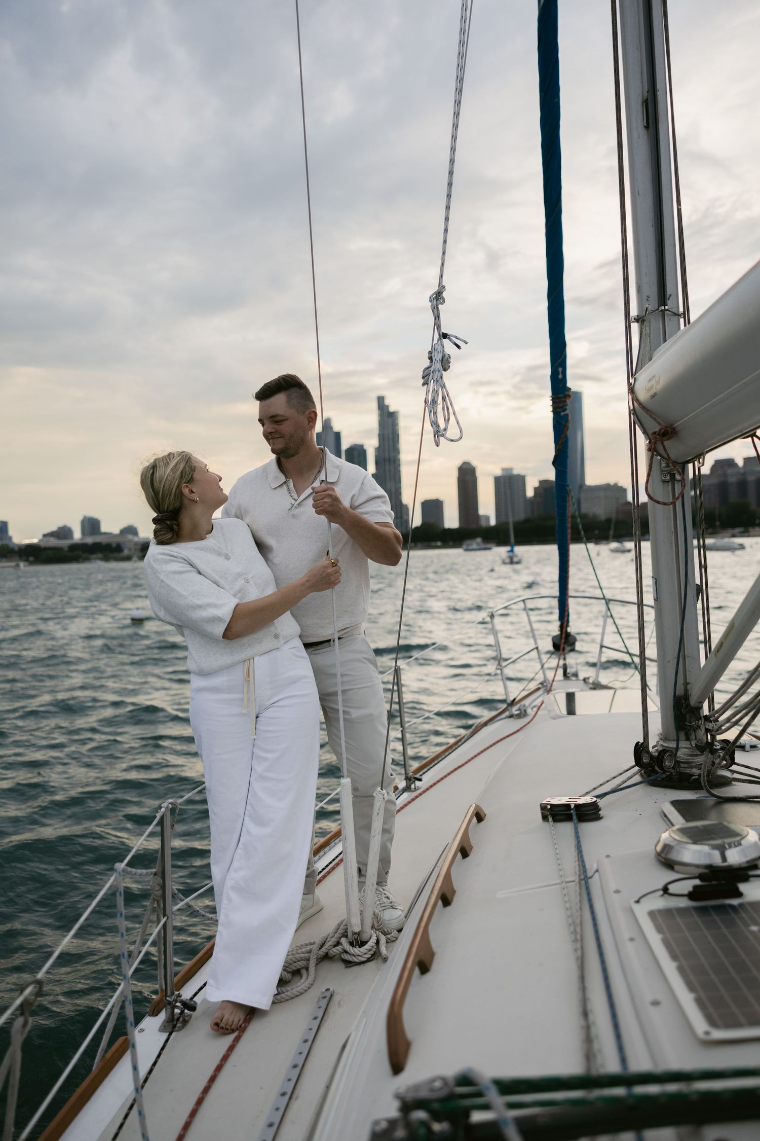 A couple in white outfits shares tender moments while sailing on a boat with city views.