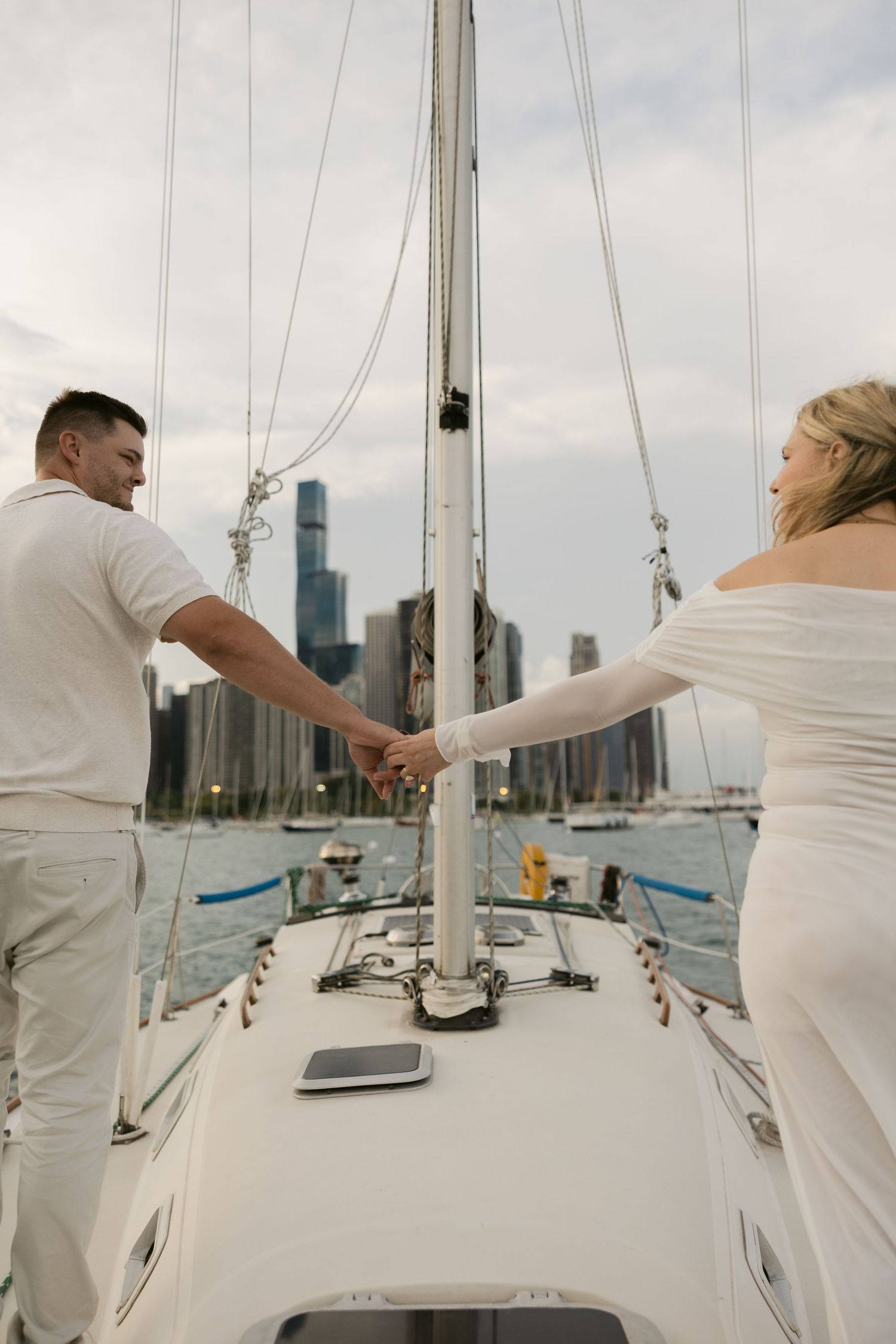 A couple navigating a sailboat together on Lake Michigan with Chicago's iconic skyline behind them.