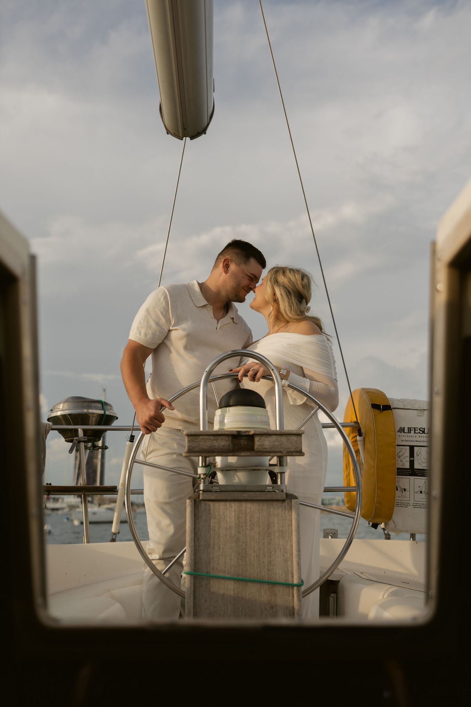 A couple sharing a tender moment at the helm of a sailboat during sunset.