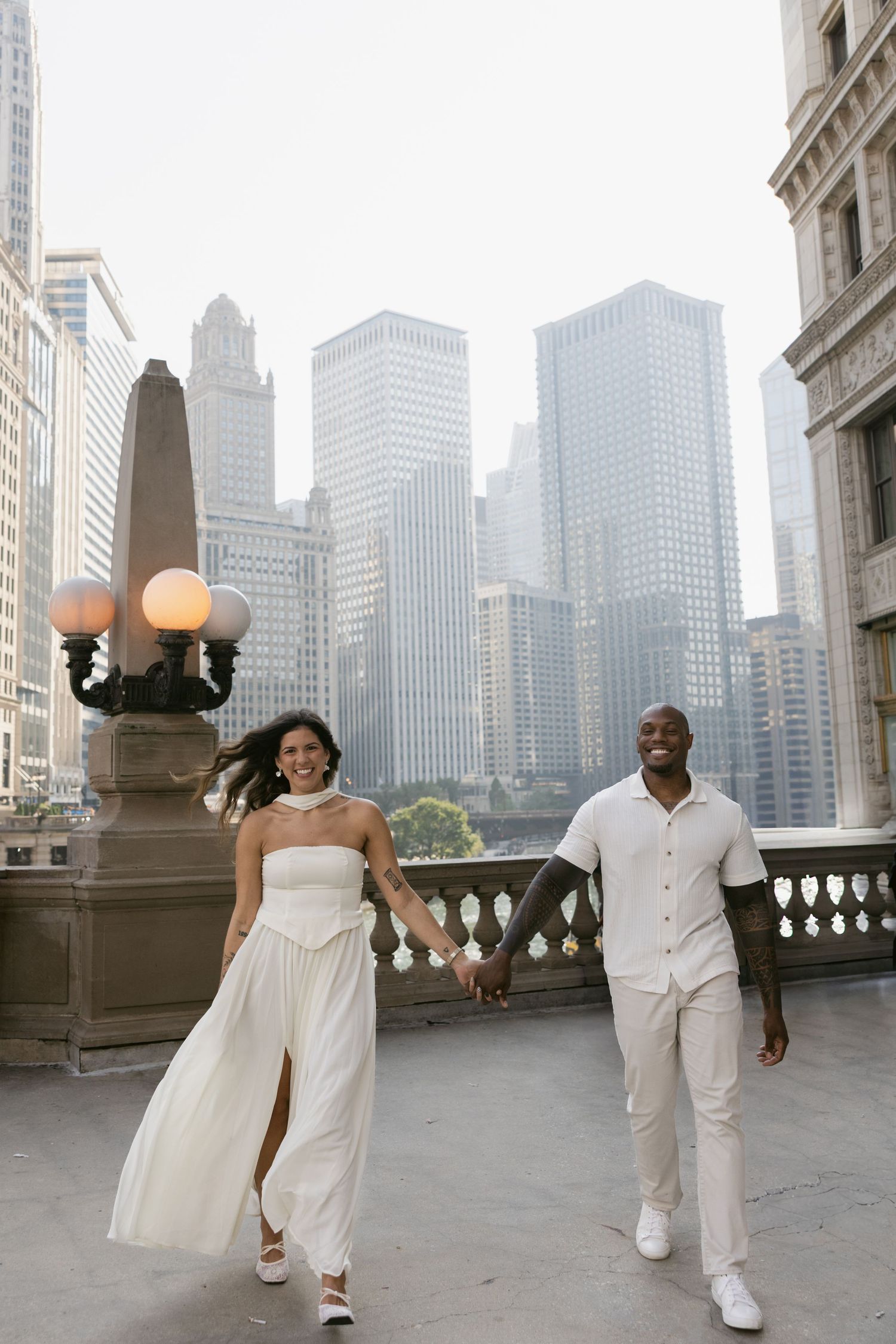 A couple in matching white outfits dances playfully on a rooftop terrace with Chicago's skyline behind them.