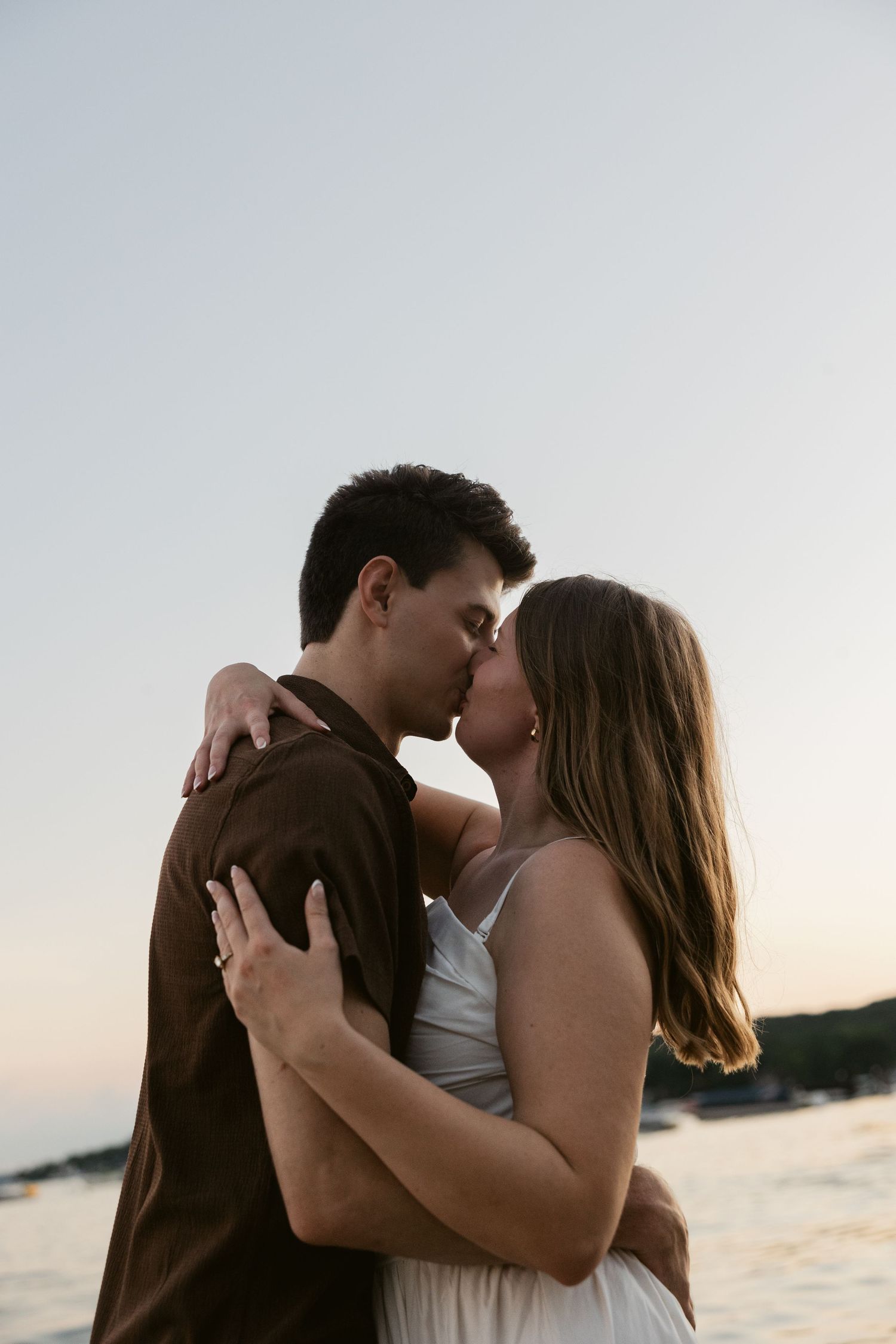 A tender sunset embrace between two people on a serene beach with soft lighting.