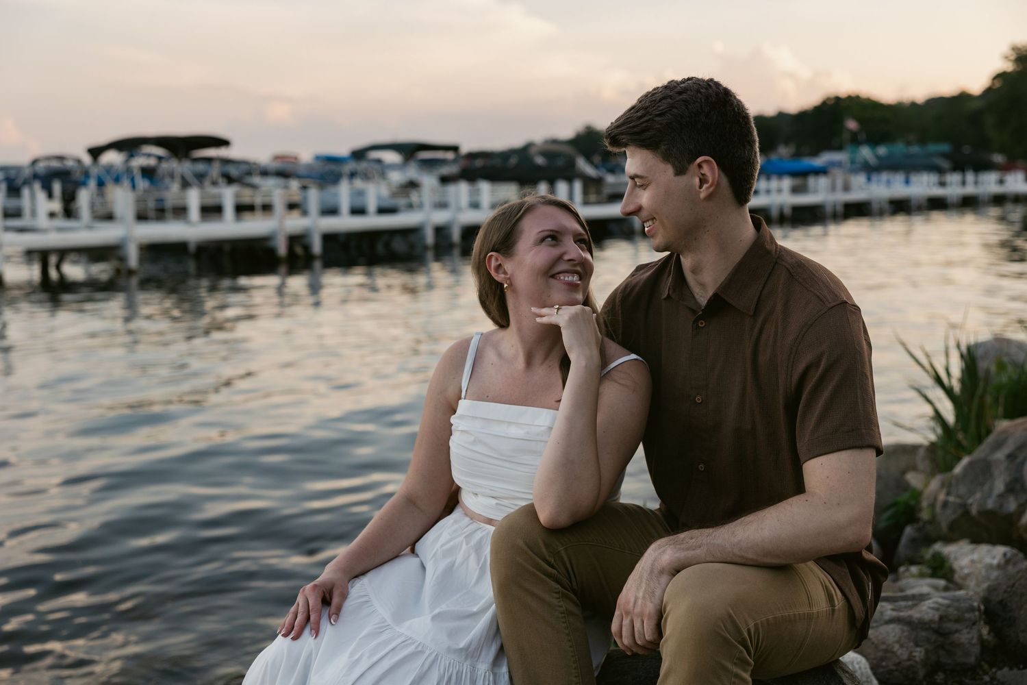 A couple enjoys intimate moments on a dock with boats and water in the background.