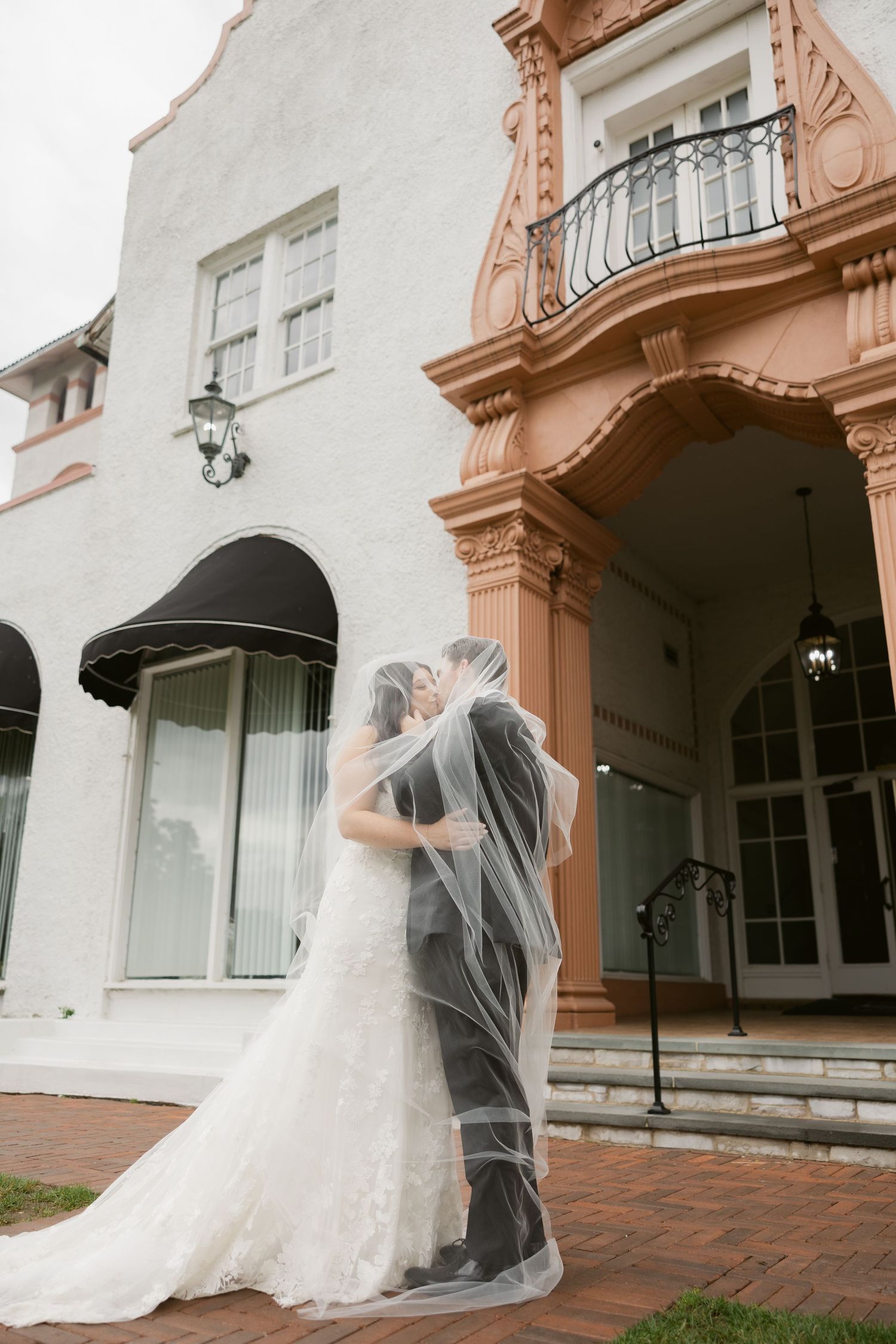 A flowing white wedding dress and veil captured in an elegant architectural setting with coral-colored columns and arches.