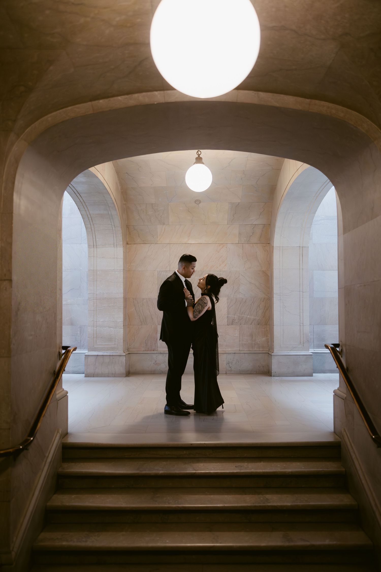 Silhouettes of a couple stand beneath a round light fixture in a minimalist architectural space.