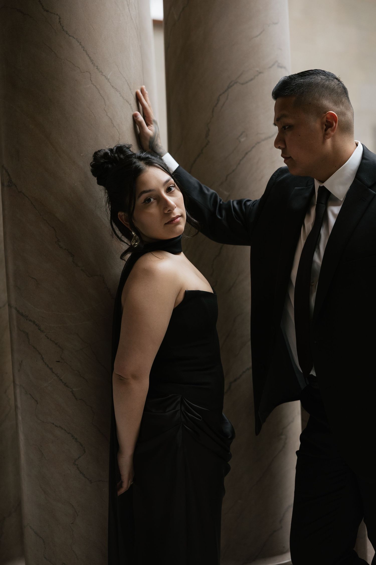 Dramatic black and white portrait between marble columns in vintage architecture setting.