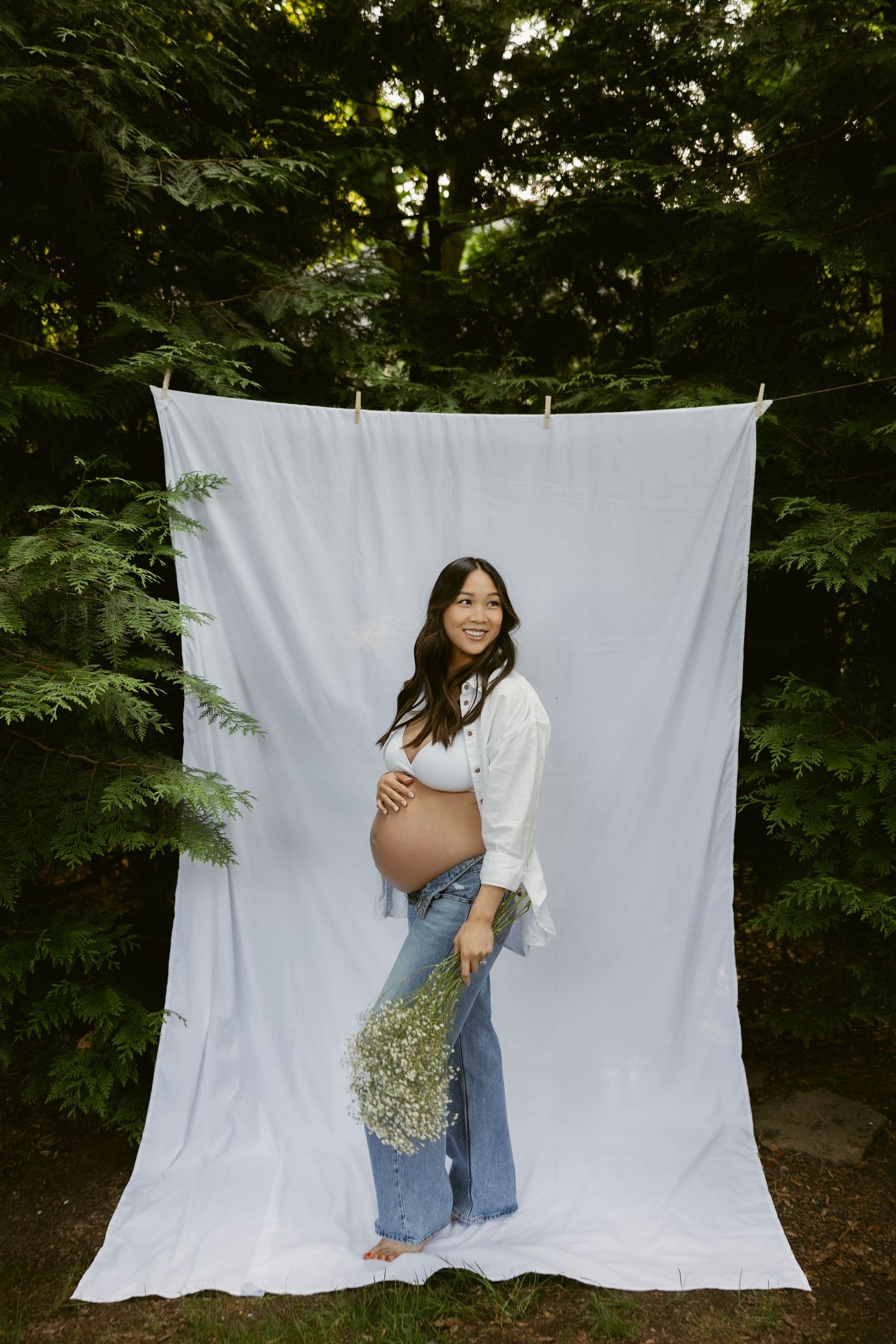 Outdoor maternity session with white backdrop and natural forest scenery.
