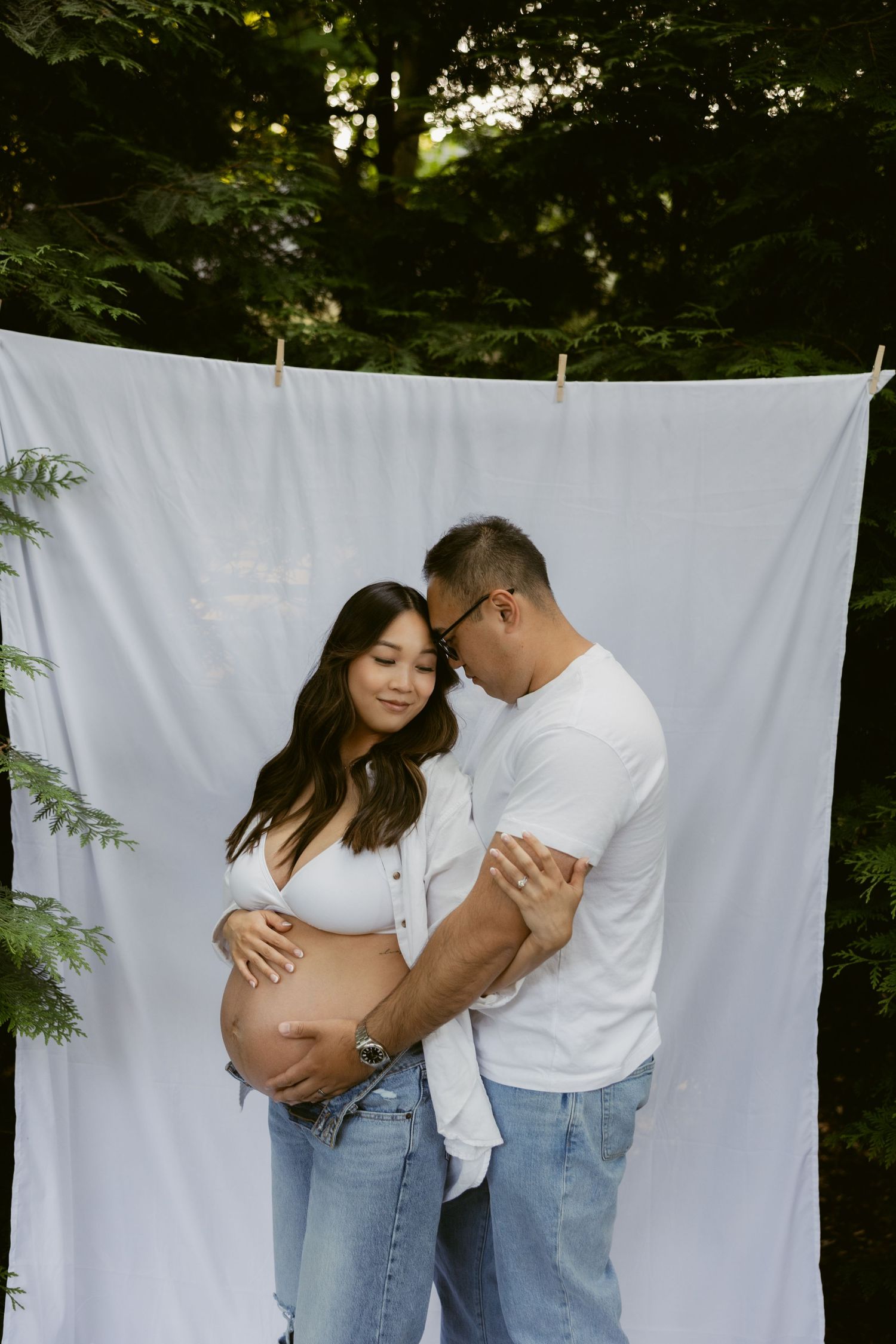 A loving maternity photo featuring a couple embracing against a white backdrop in a forest setting.