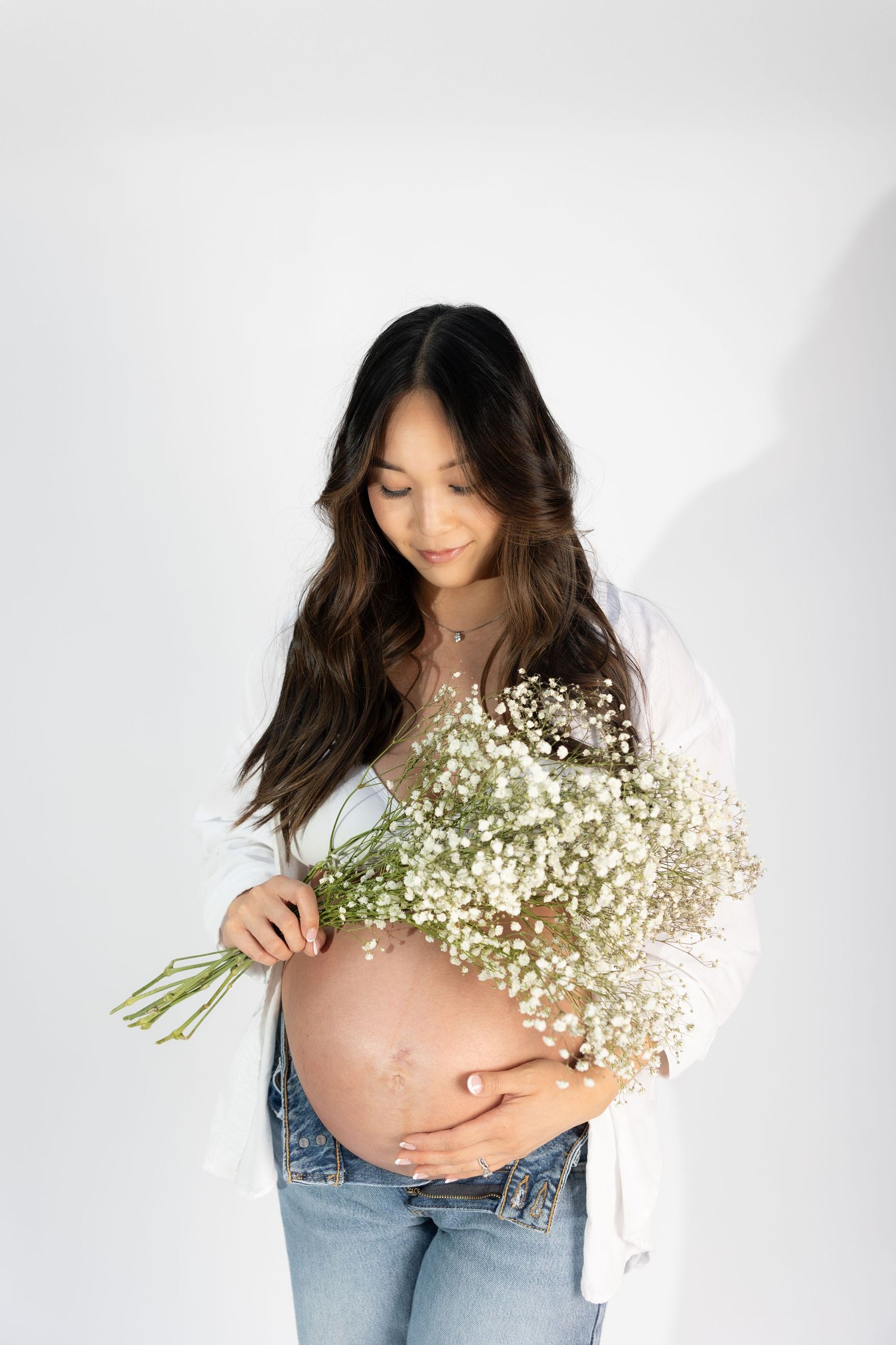 Side view of pregnant woman in casual attire holding delicate white flowers.