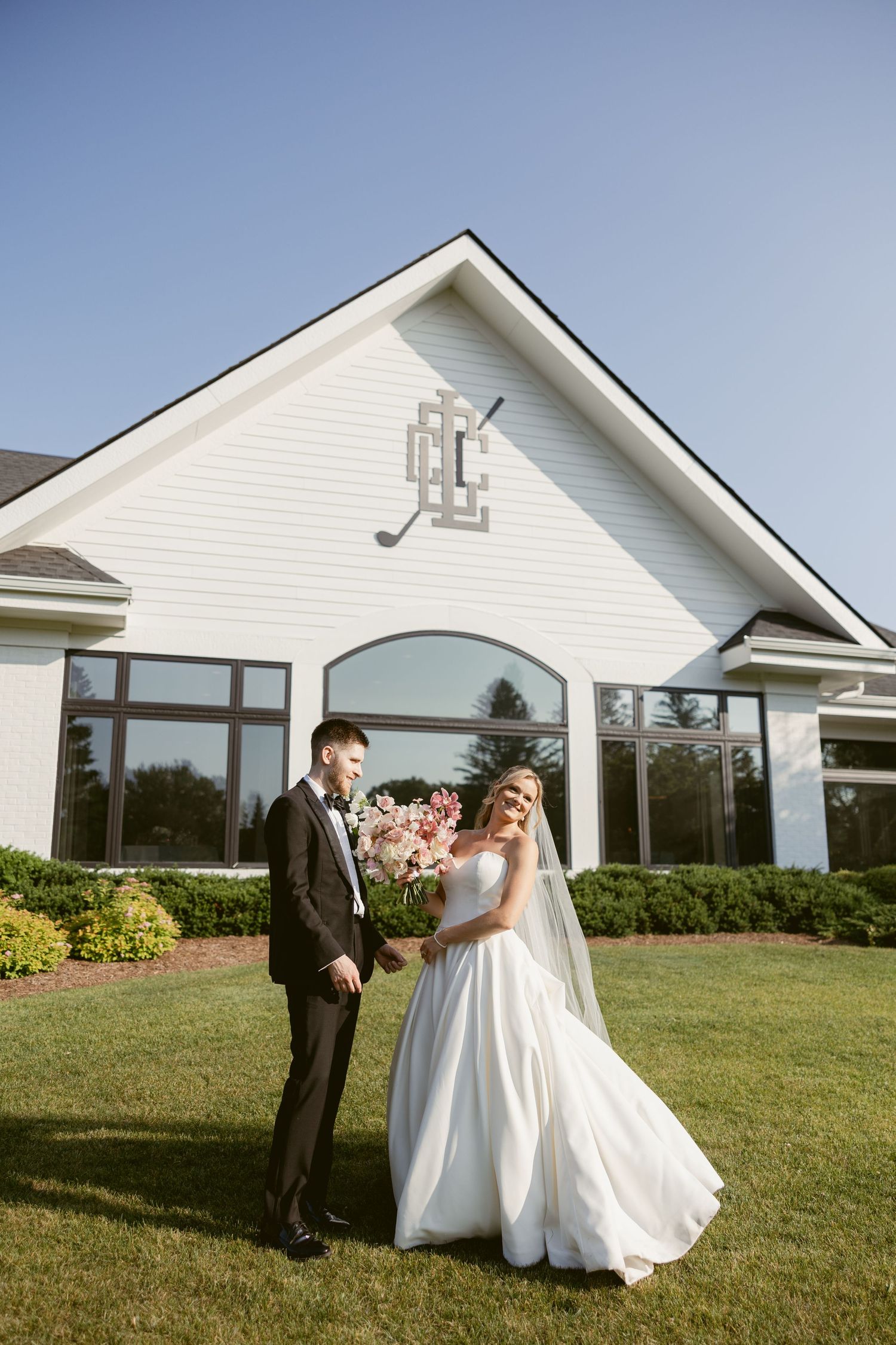 Newlyweds pose for portraits outside a classic white wedding venue with large windows.