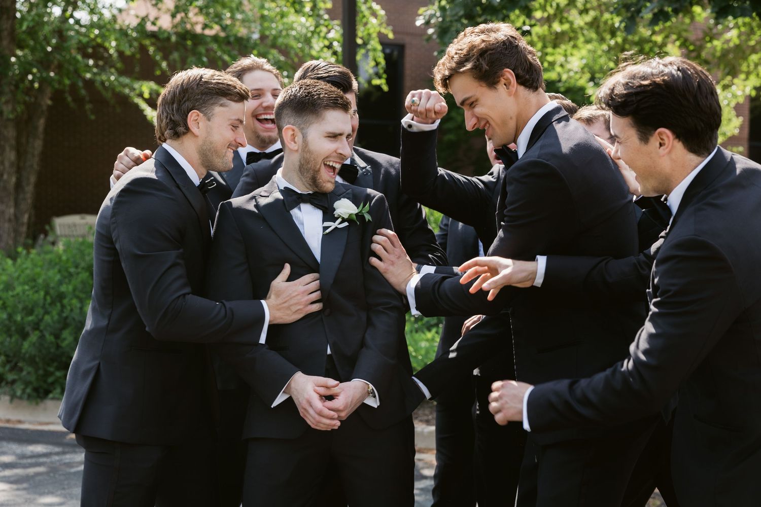 A group of groomsmen laugh together while wearing black tuxedos during a candid moment.