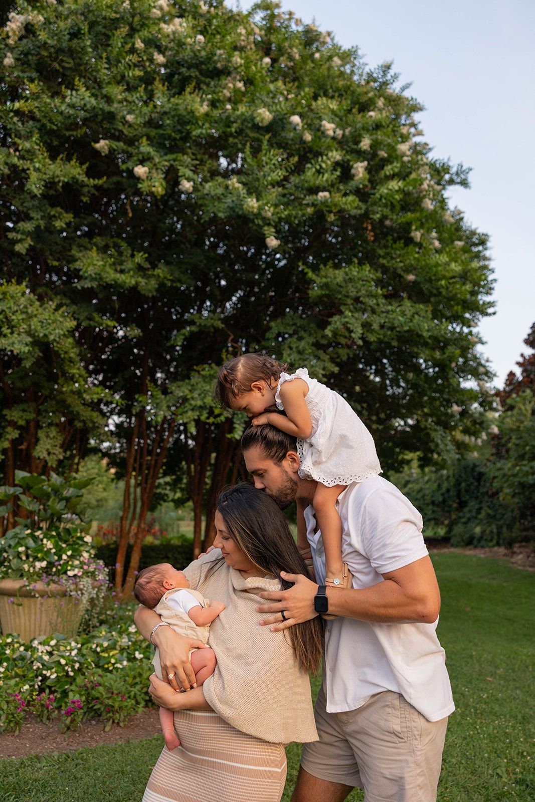 A loving family shares a tender moment together under a blooming tree in a garden setting.