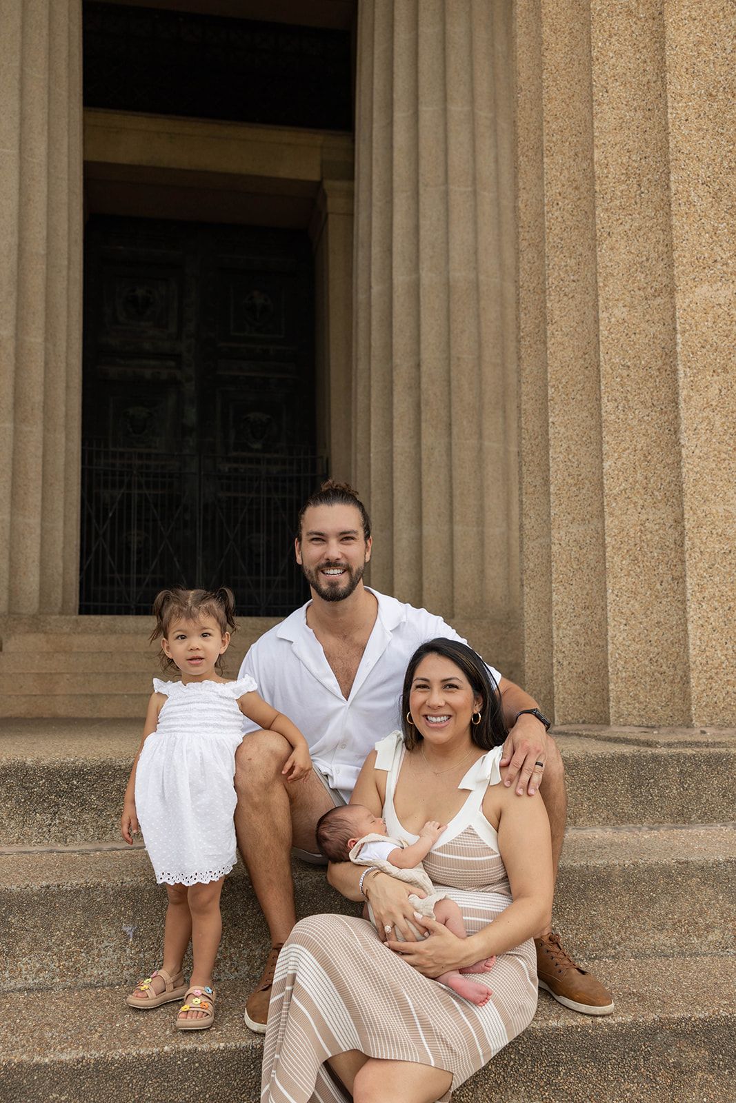 Family of four poses on stone steps of classical building during portrait session.