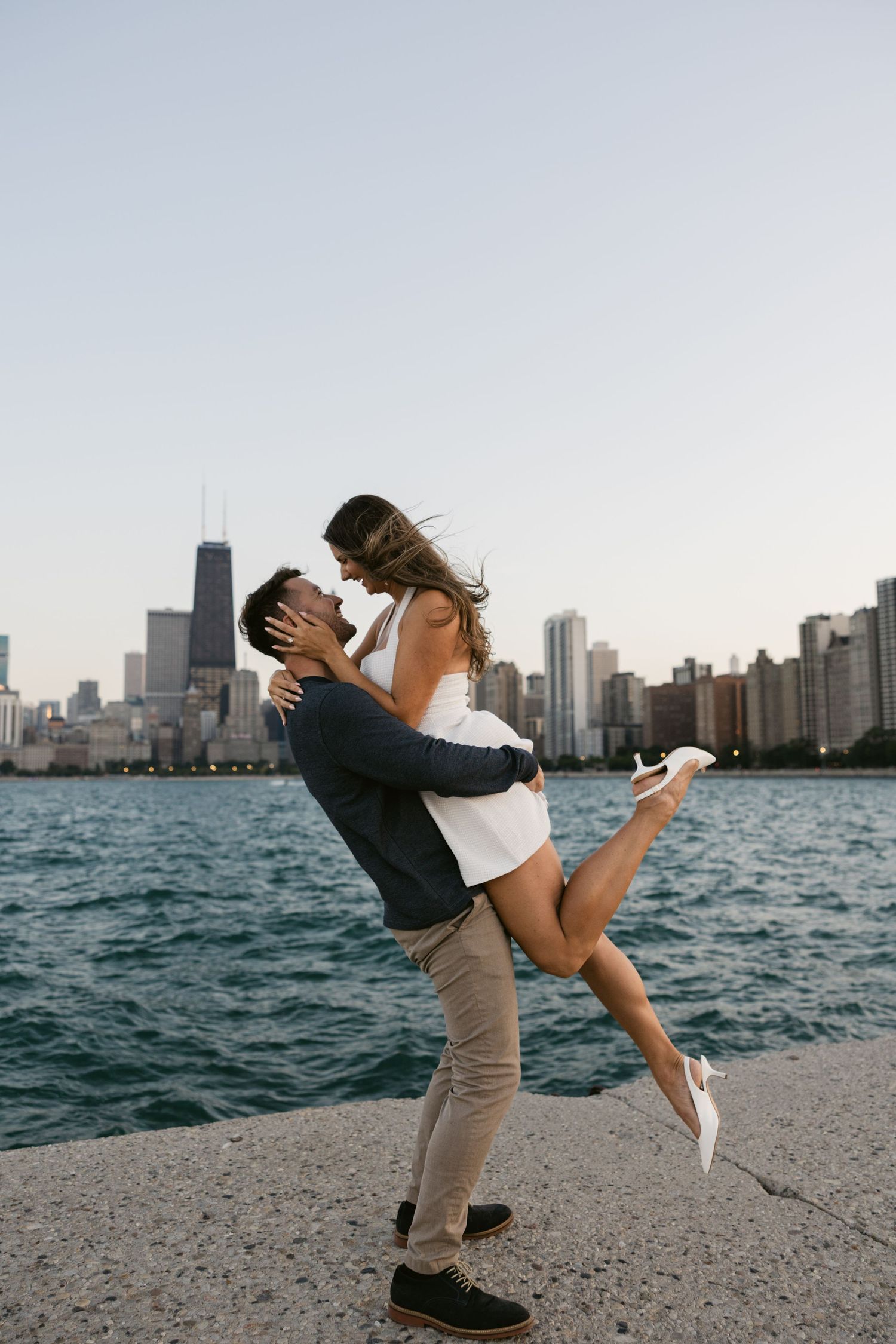 A playful couple performs a dramatic dip pose with the Chicago skyline behind them.